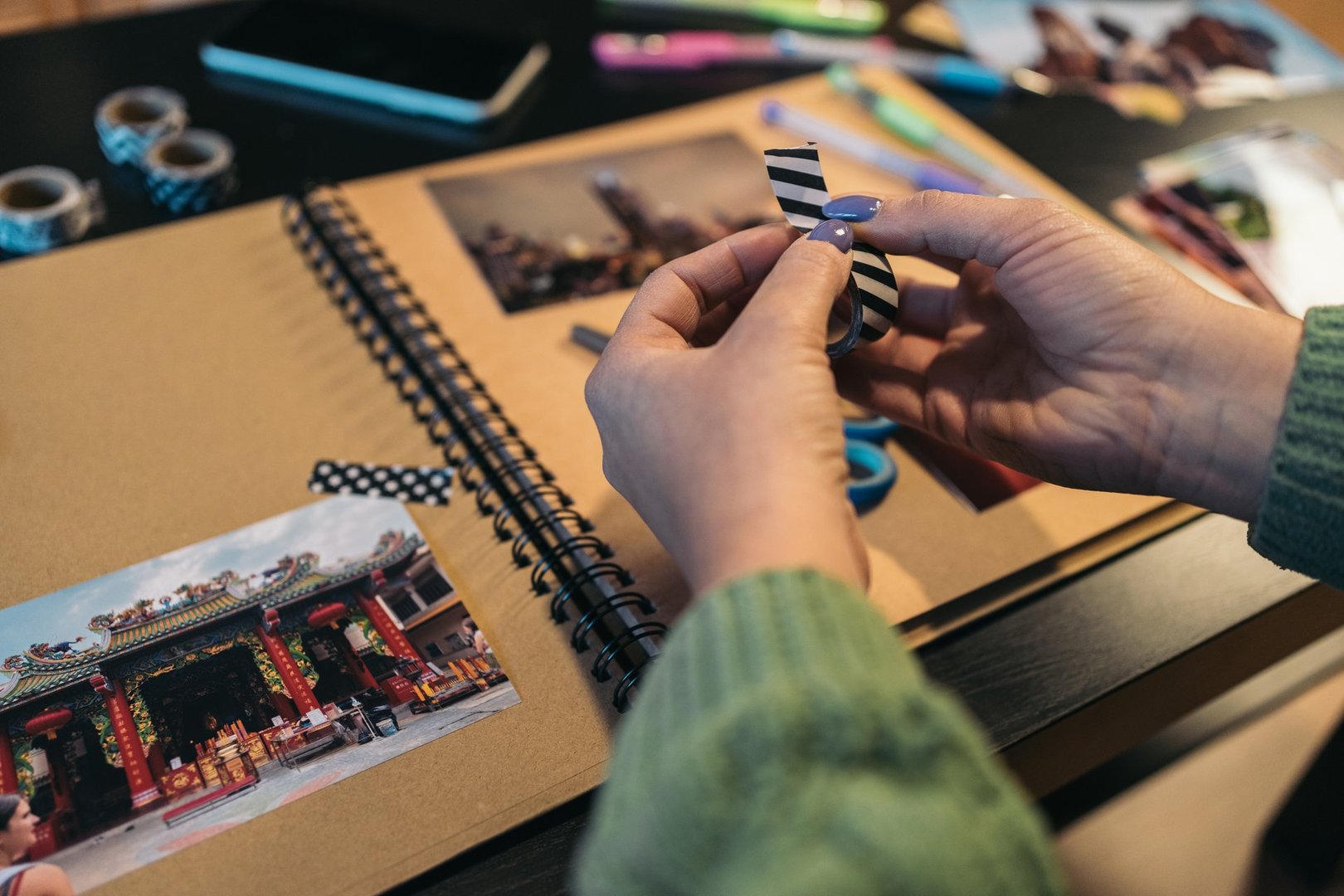Middle-aged woman's hands holding a roll of washi tape that she is going to use to paste a photo onto her handmade kraft travel album.