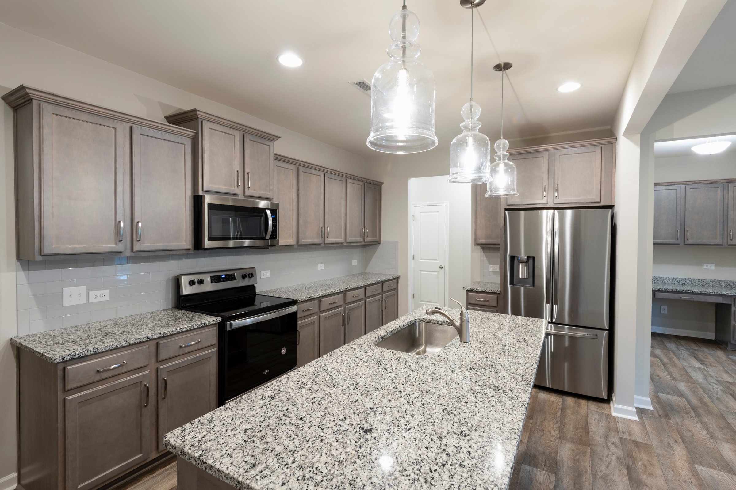Modern kitchen with stainless steel appliances, granite countertops, and stylish cabinetry. Open layout with a spacious island and hanging glass pendant lights. Investment, renting, or homeownership concept.
