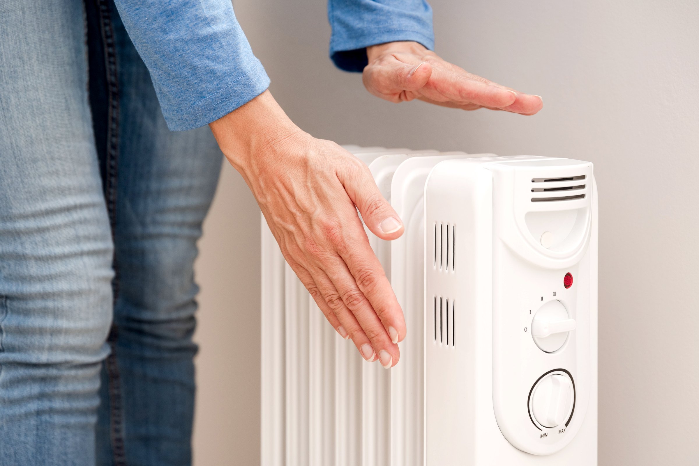 Person warming hands over white electric radiator