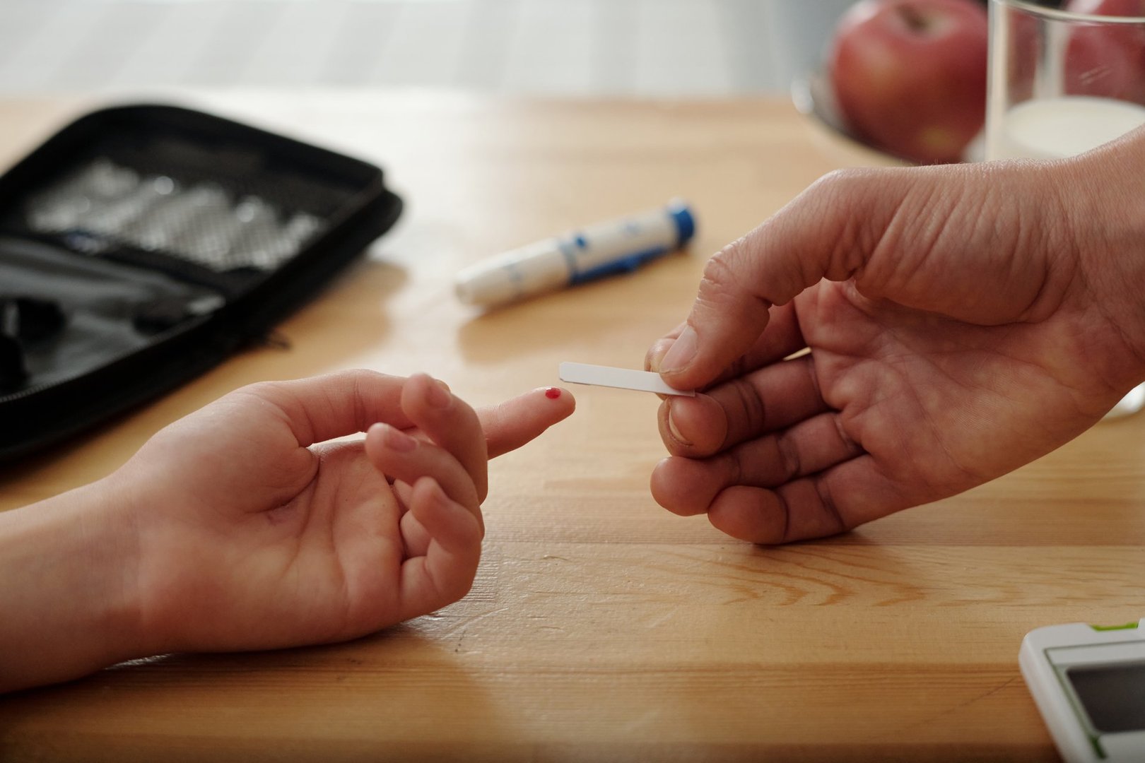 Side view closeup of child with diabetes doing blood test using strips while monitoring glucose levels with hands on wooden table copy space