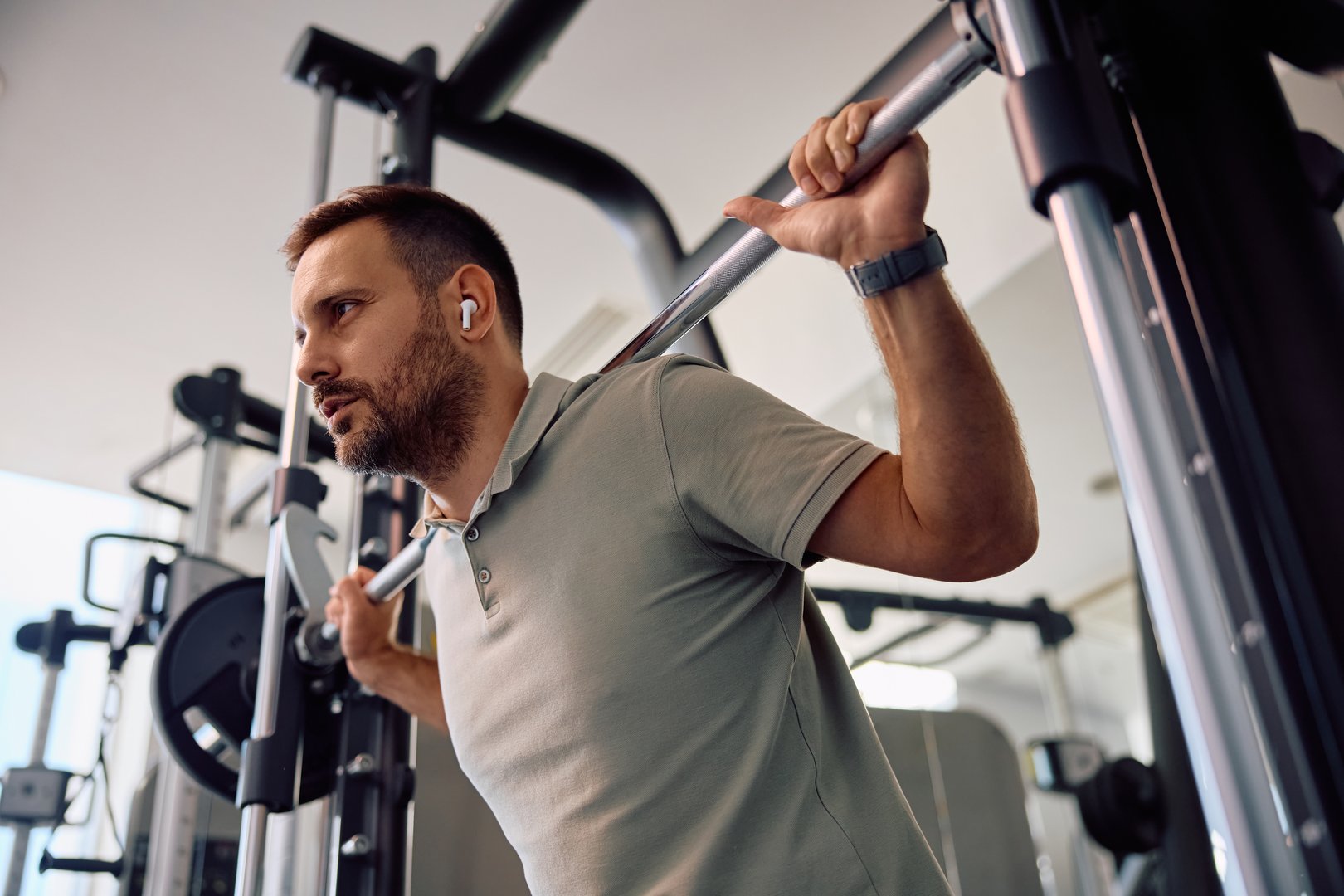Low angle view of athletic man using barbell while exercising strength on sports training in health club.