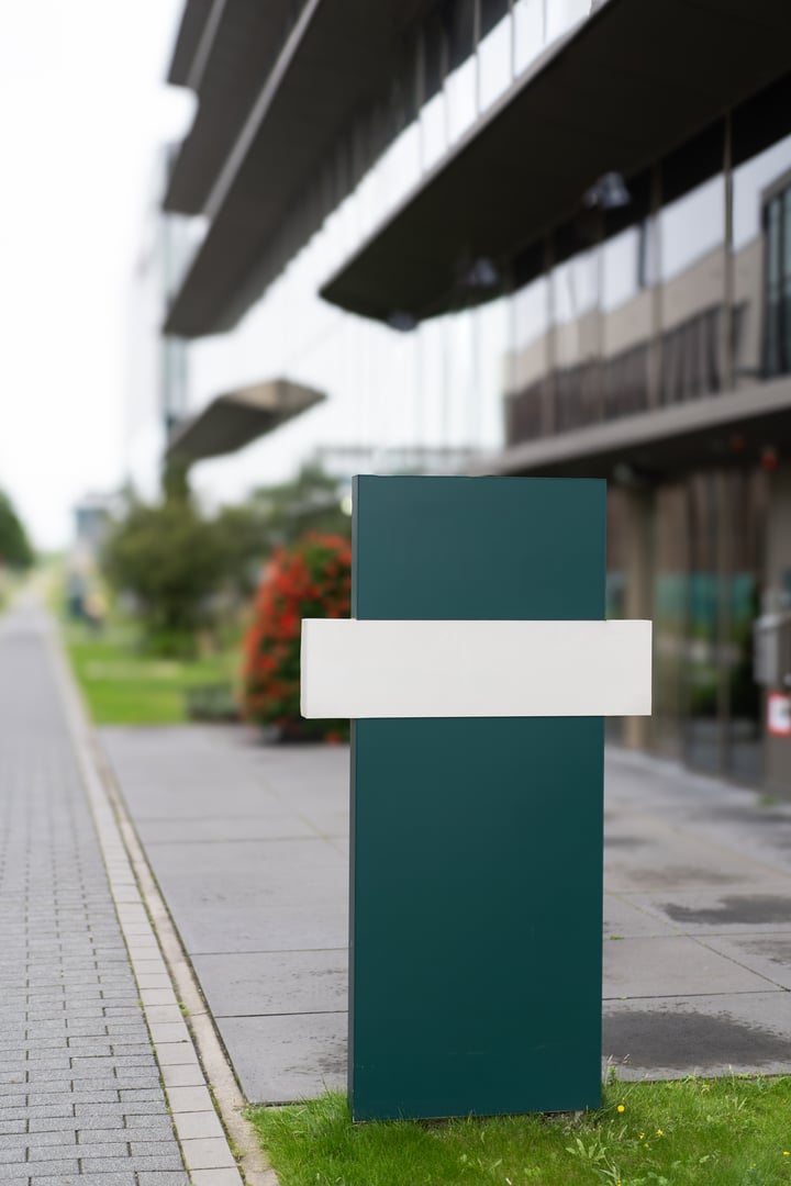 A green and white modern signpost standing outside in front of a contemporary office building during daytime