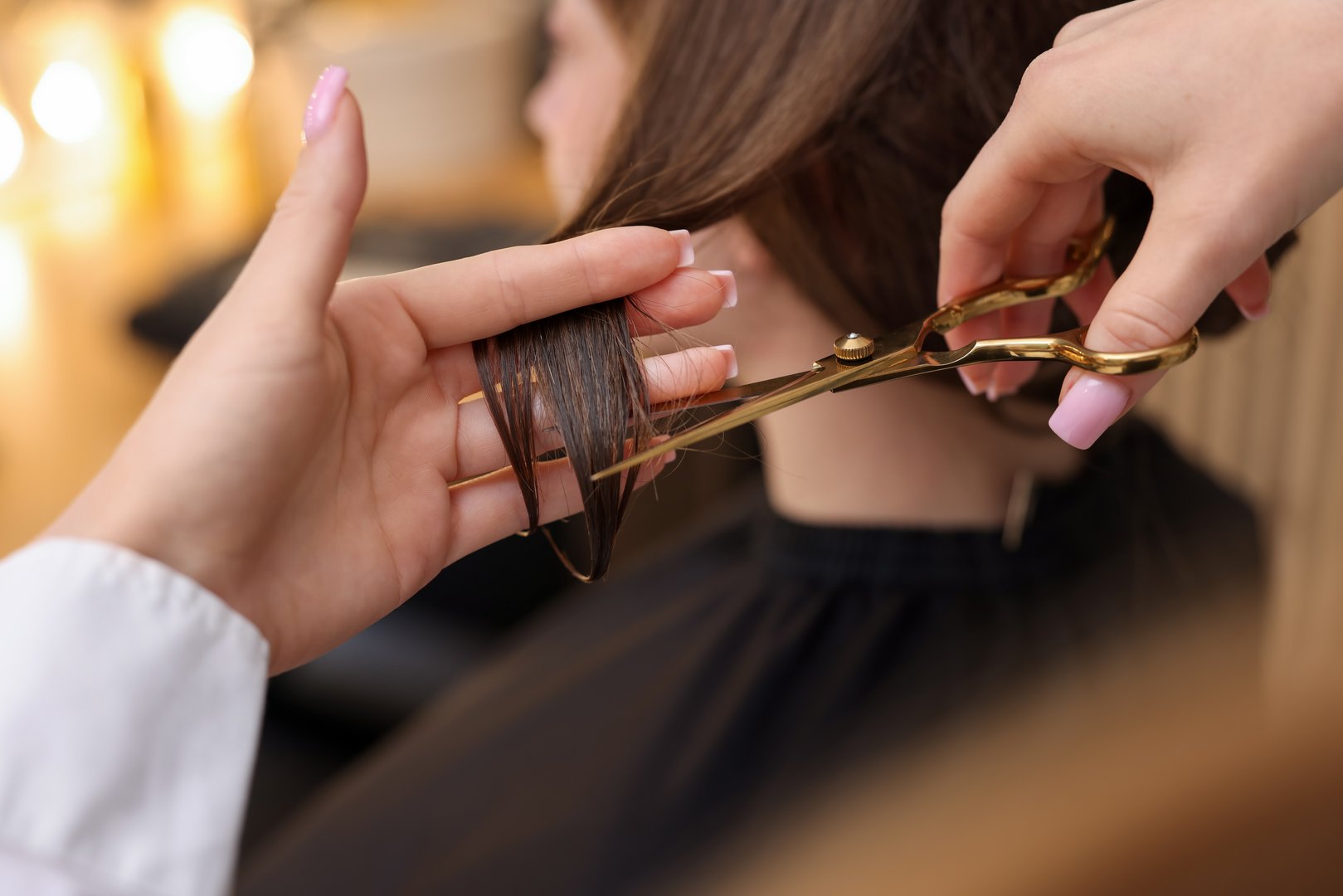 Hairstylist cutting client's hair with scissors in salon, closeup