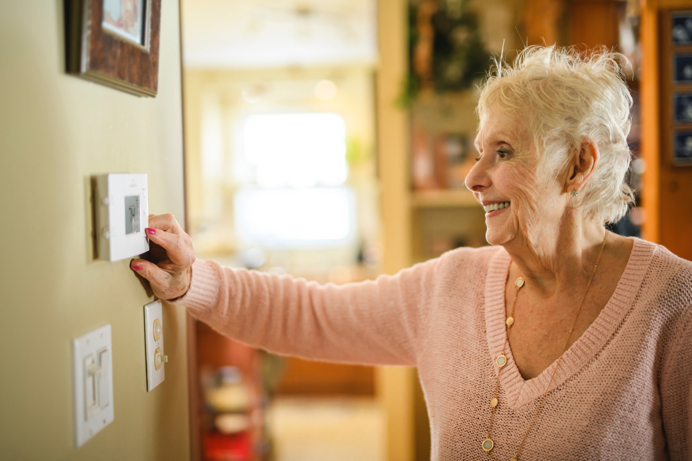 A senior lady posing at home portrait close to a window using thermostat