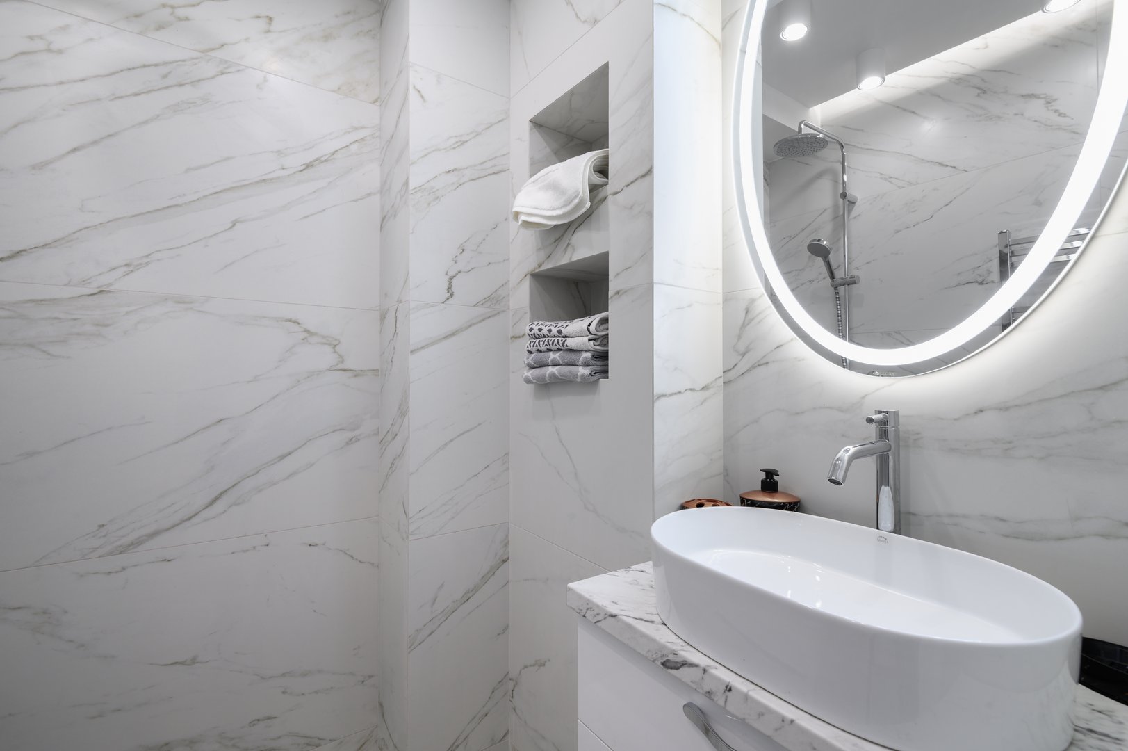 White bathroom interior with marble tiles on the walls and a round mirror