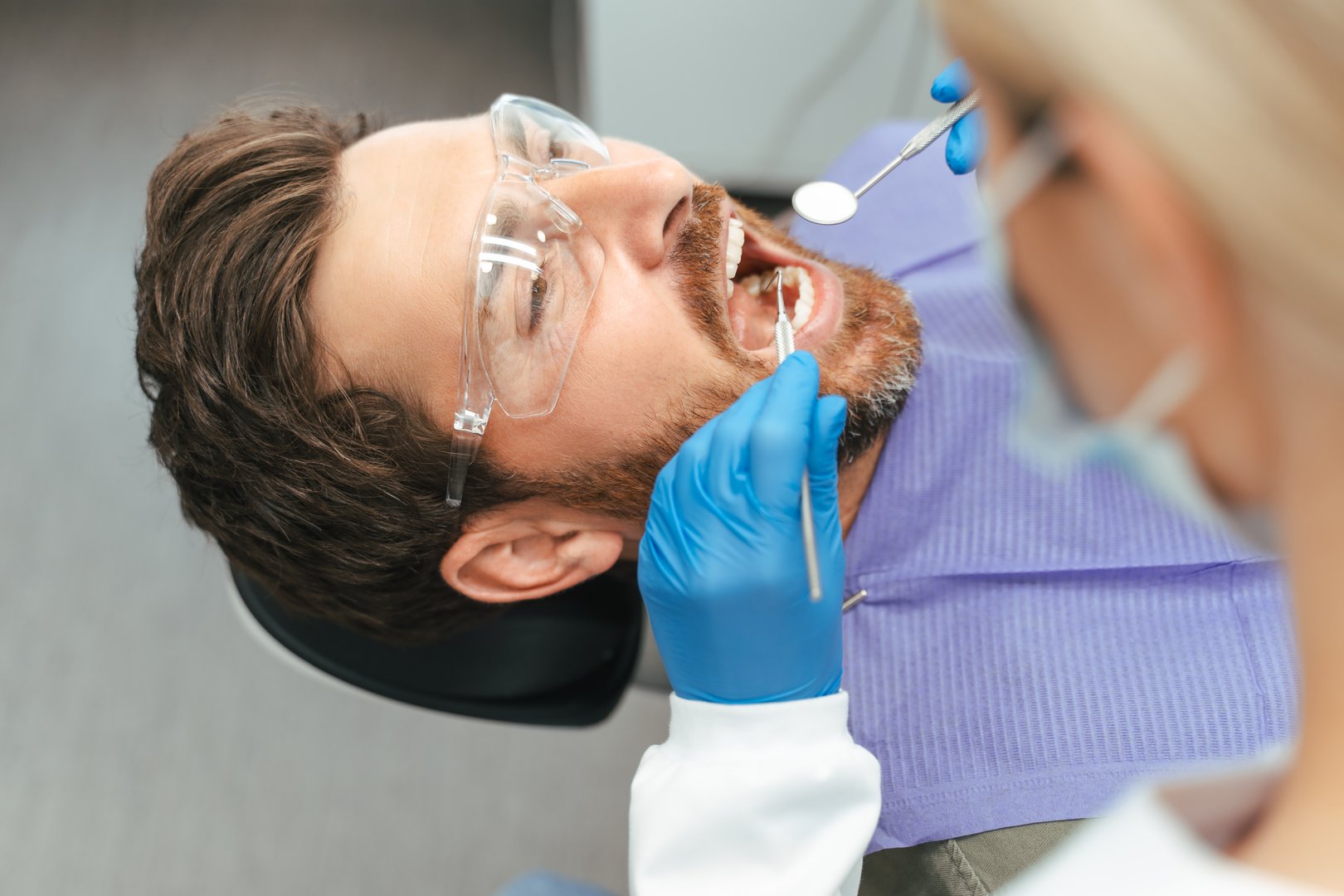 Dentist wearing blue gloves examining patient teeth with dental tools in a dental clinic