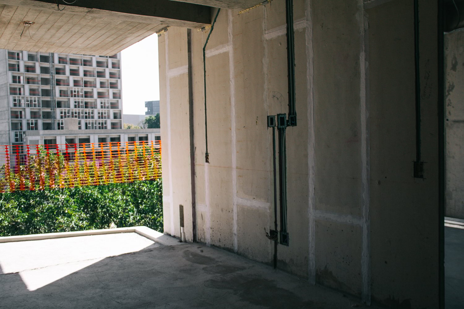 Interior of an unfinished building with exposed concrete walls, electrical boxes, and a view of another building outside.