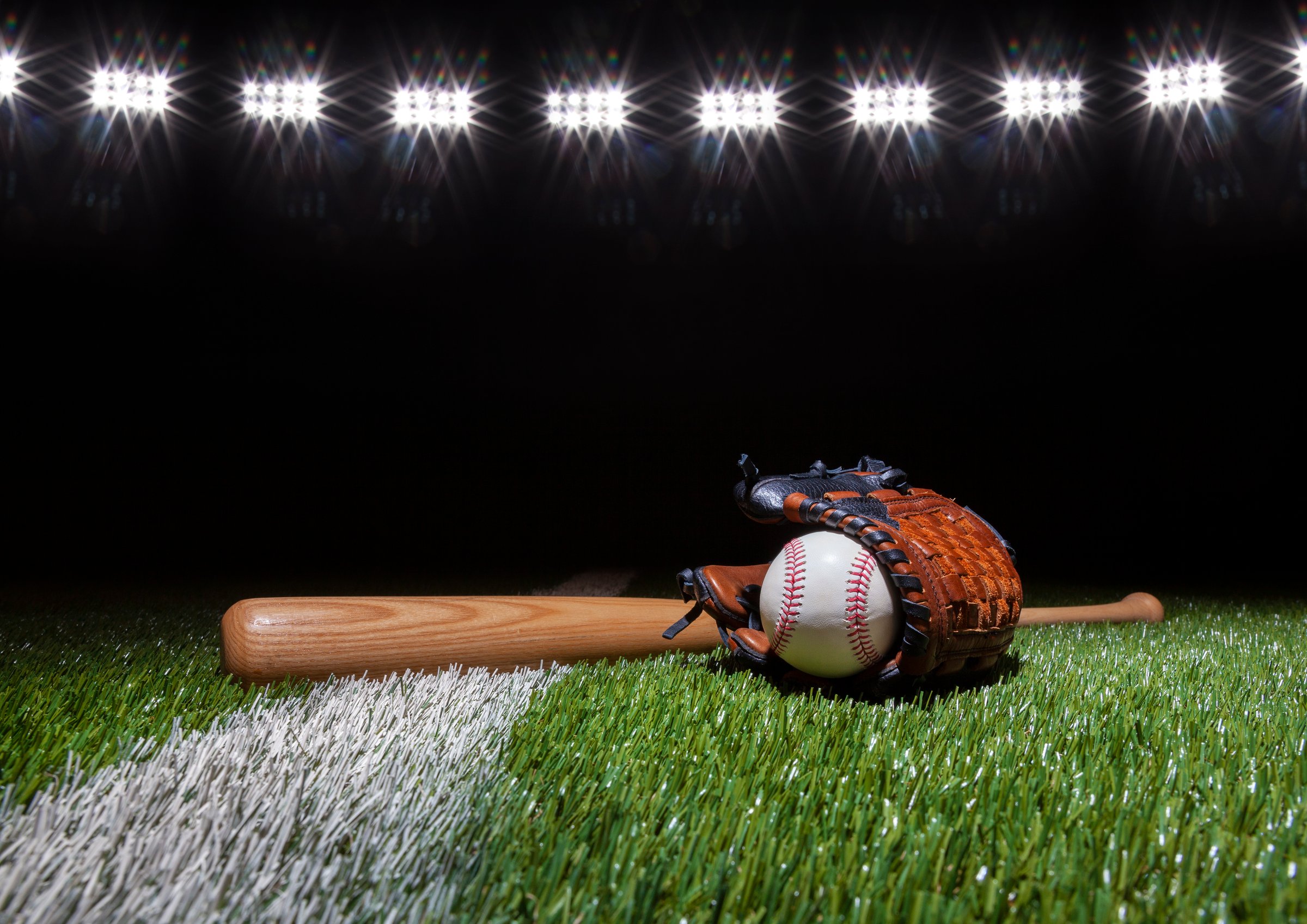 Baseball batt glove and ball low angle on grass field with stripe below lights at night