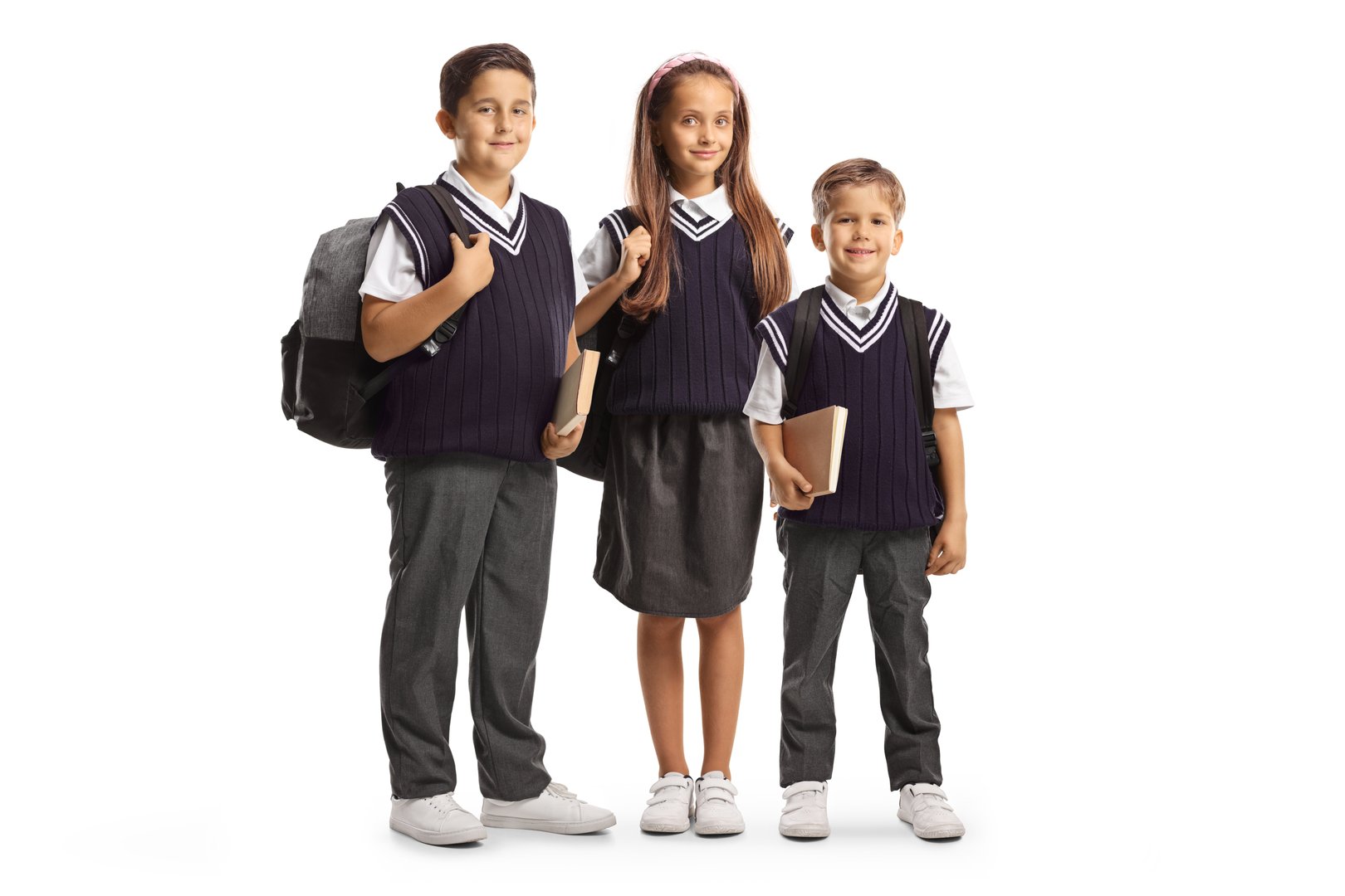 Two boys and one girl in school uniforms carrying backpacks isolated on white background