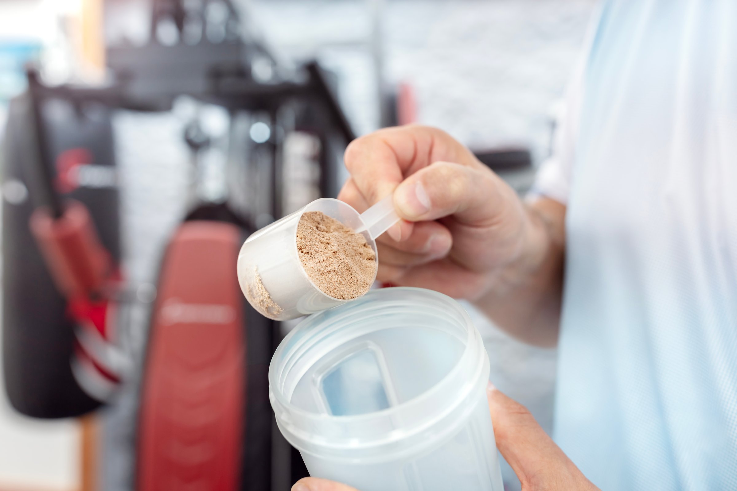 Whey protein powder in scoop and shaker bottle, man training and preparing protein shake drink in gym