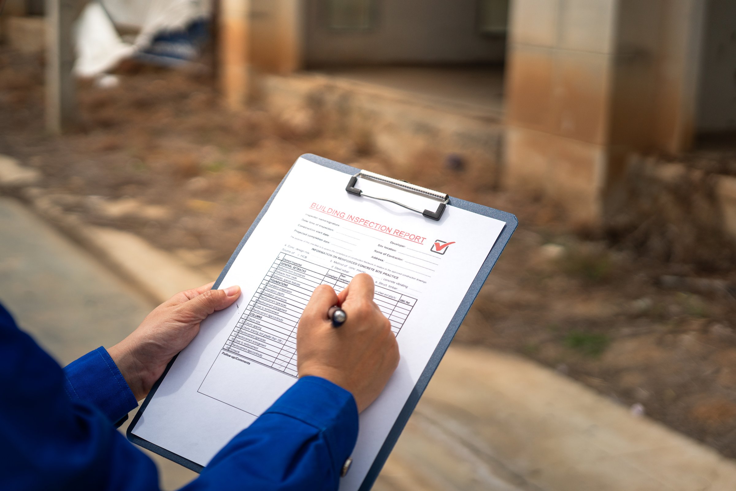 A construction foreman is checking on building quality checklist report during inspecting at the house construction site (as background). Industrial working scene, close-up with selective focus.