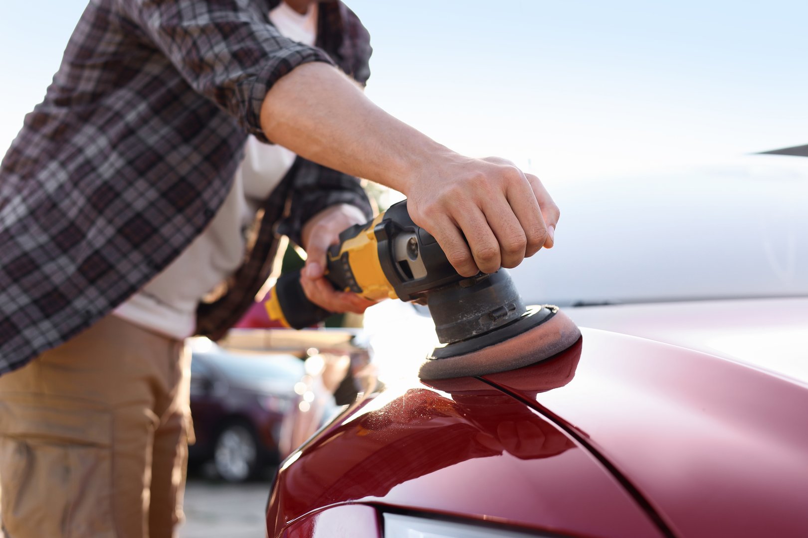 Man polishing car hood with orbital polisher outdoors, closeup