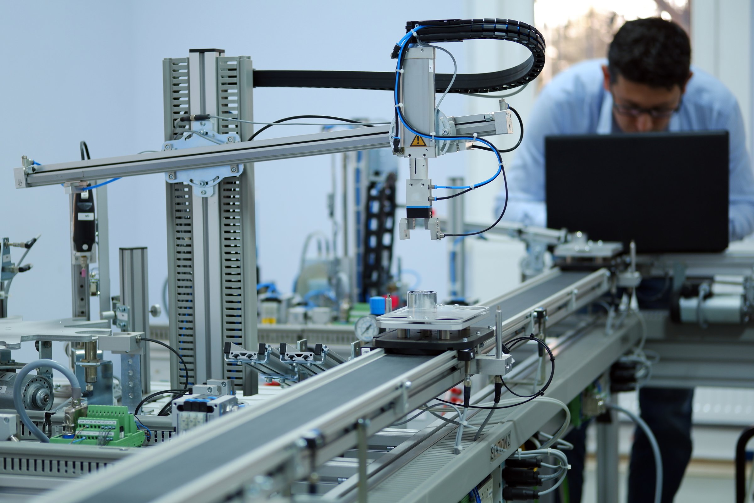 Focus on Gripper which picks up the product from an automated car and programming engineer at the background. Industry 4.0 workshop in an automation education center. Engineer is programming PLC.
