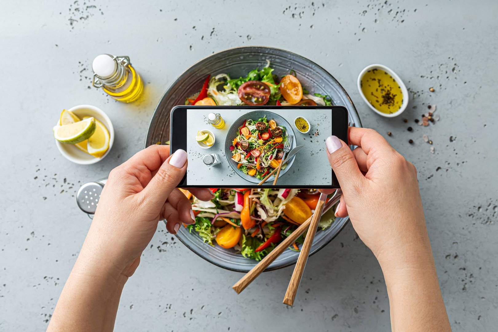 Woman taking photo of fresh, spring, vegetable salad with smartphone. Using phone while eating lunch. Lifestyle trend - posting and sharing food pictures (images) on social media.