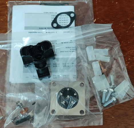Electronic components kit with connectors, screws, and metal plate in plastic bags on a wood surface.
