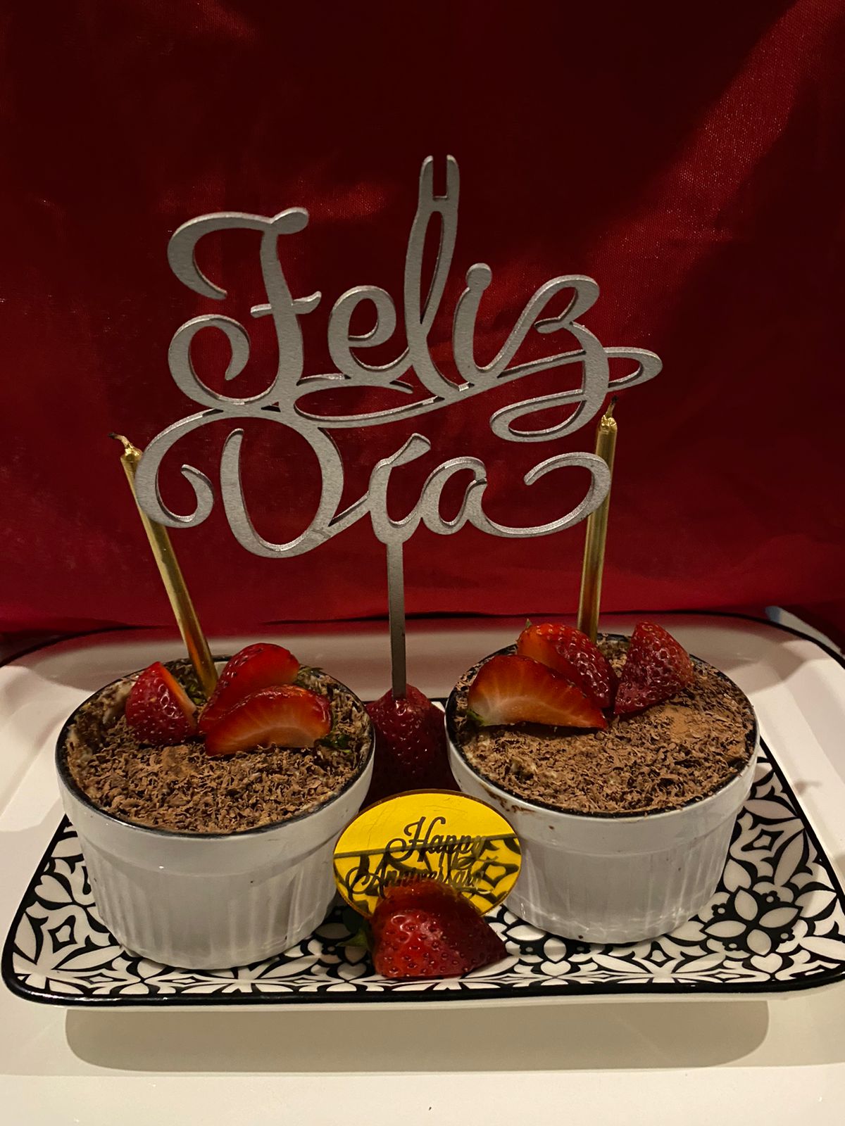 Two dessert cups topped with chocolate shavings and strawberries, with Feliz Día decoration on a decorative plate.