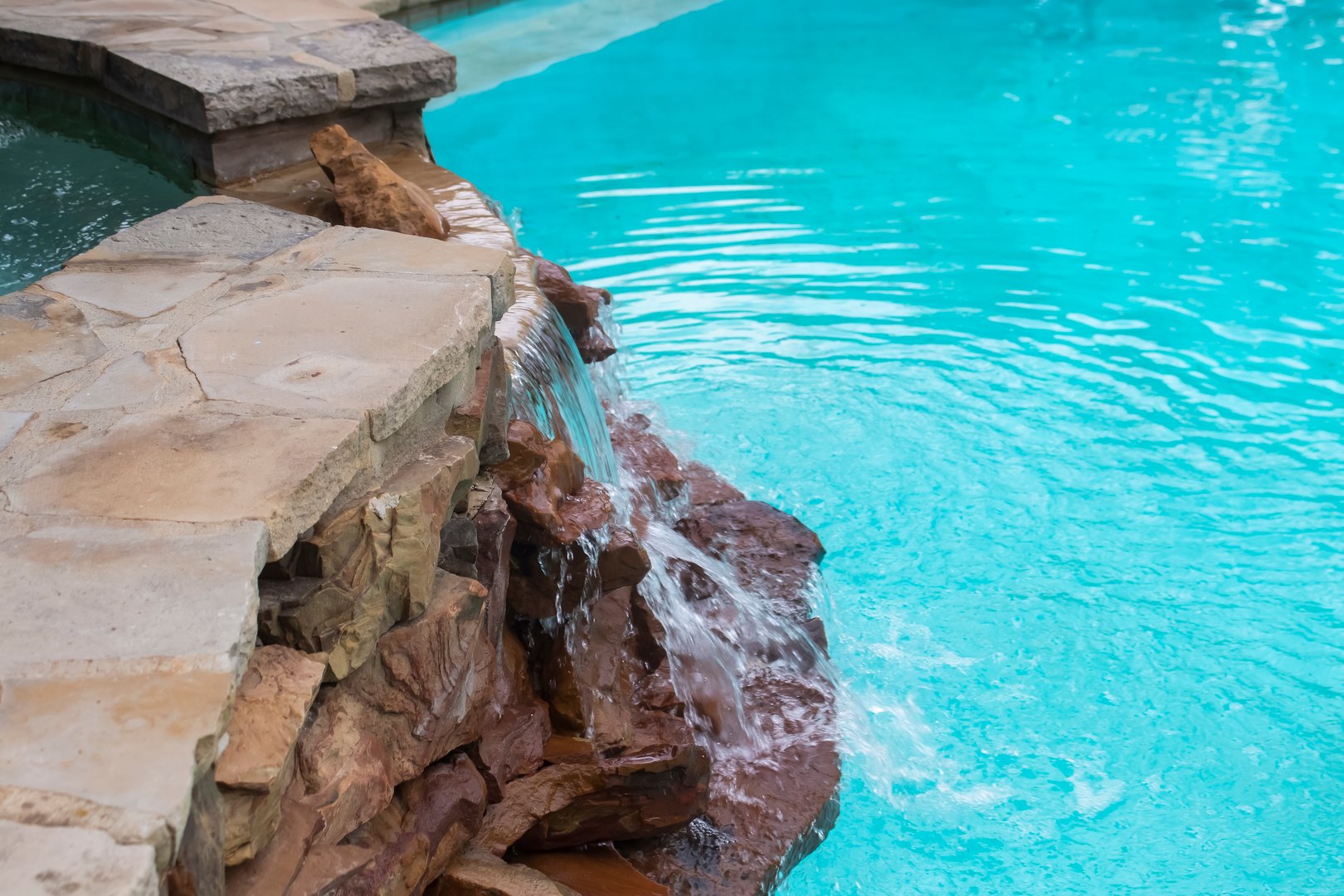 Waterfall over rocks from hot tub on higher level down to swimming pool