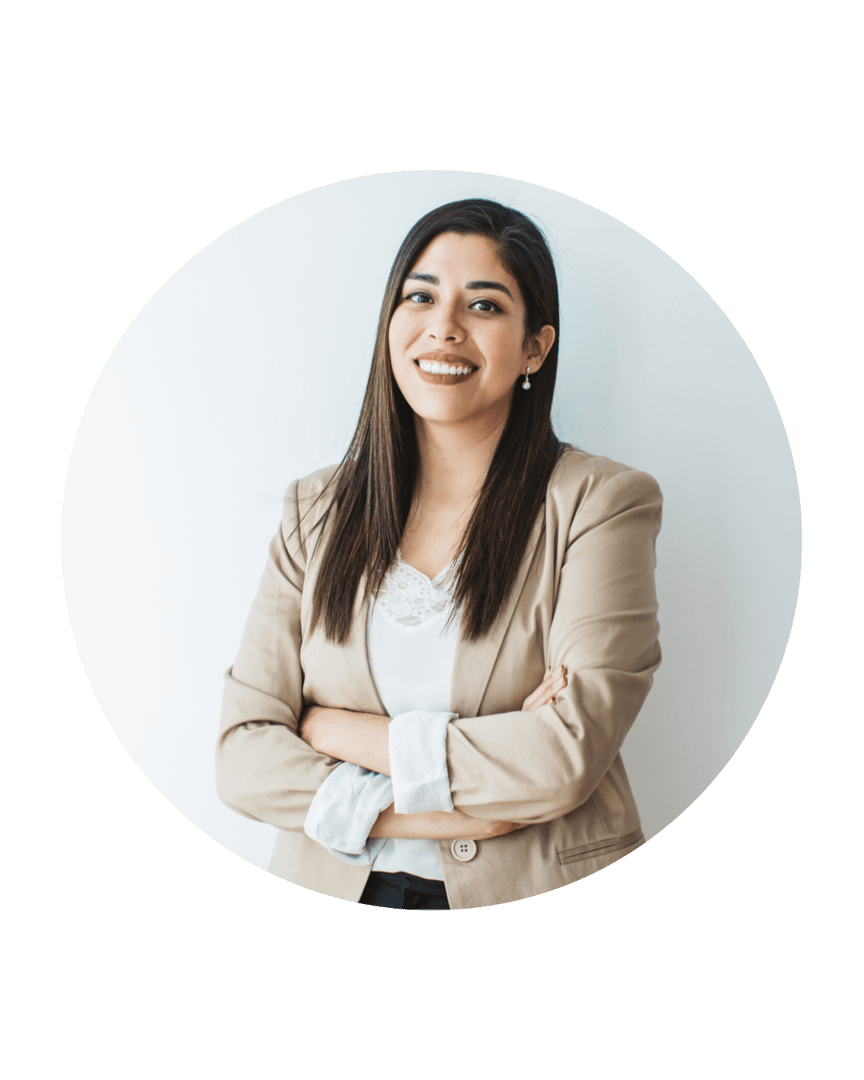 Smiling woman with long hair in a beige blazer, standing with arms crossed against a white background.