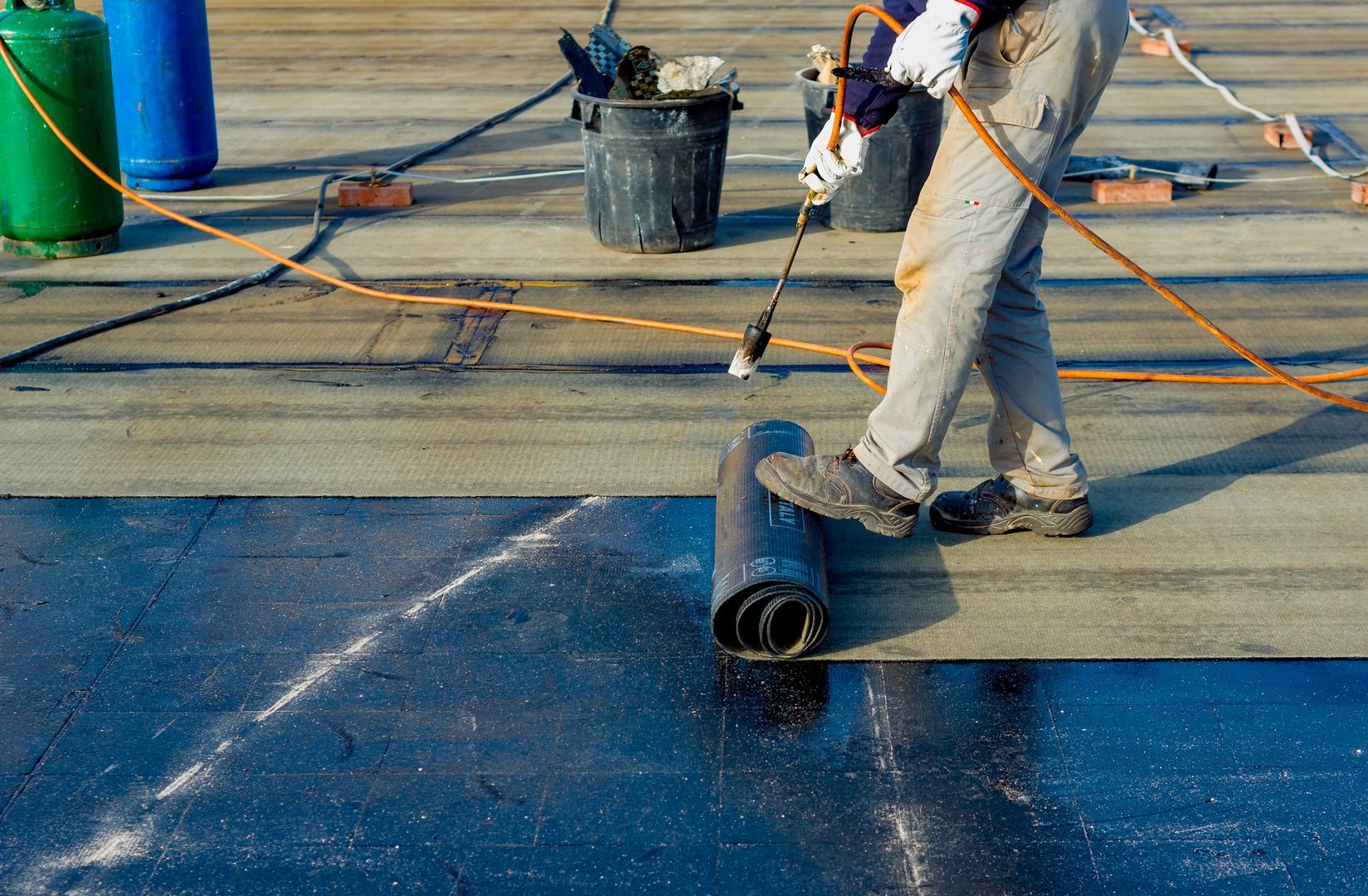 Worker preparing part of bitumen roofing felt roll for melting by gas heater torch flame
