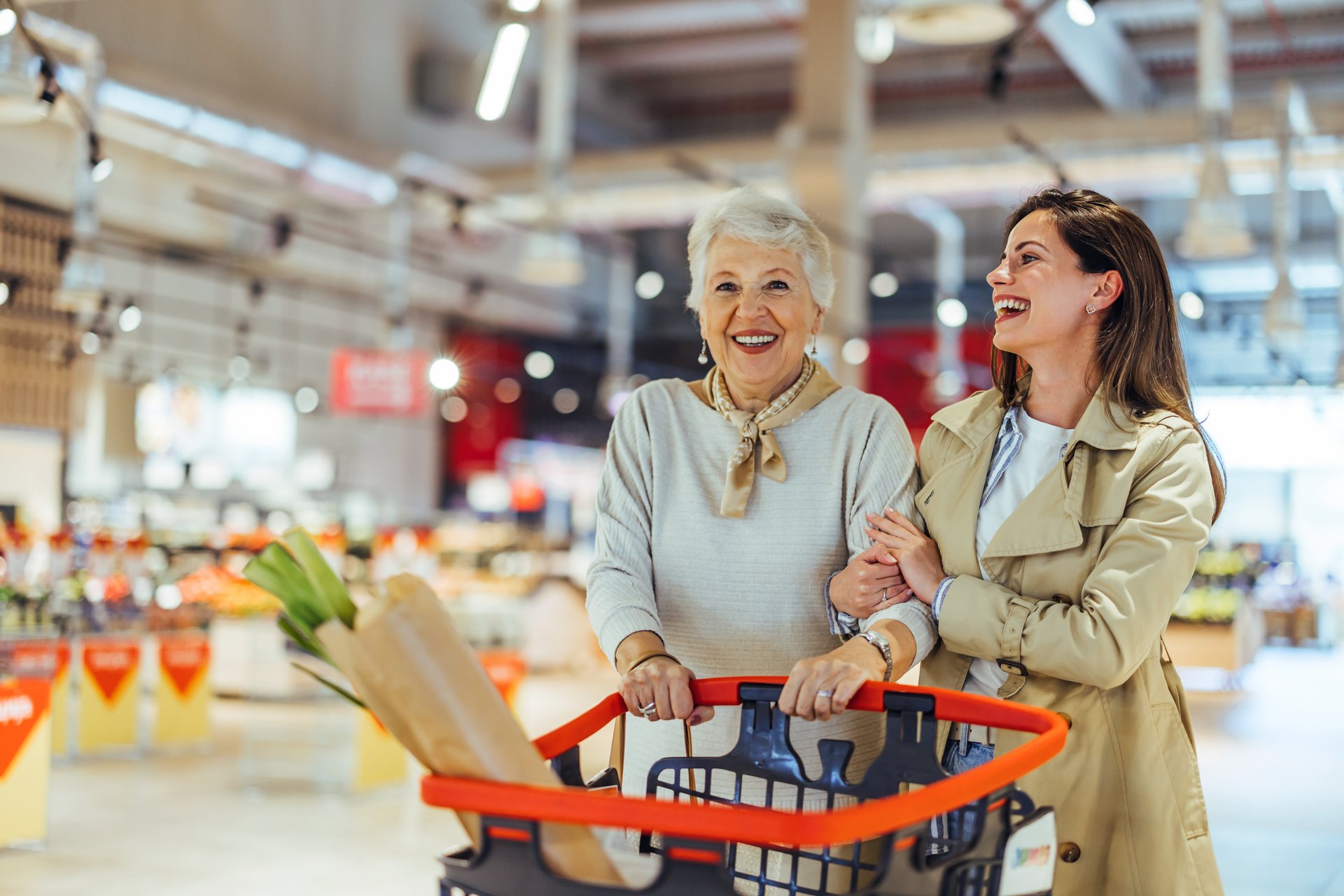 Senior woman and young woman sharing a joyful moment while grocery shopping in a supermarket. They appear happy and engaged in a leisurely shopping experience.