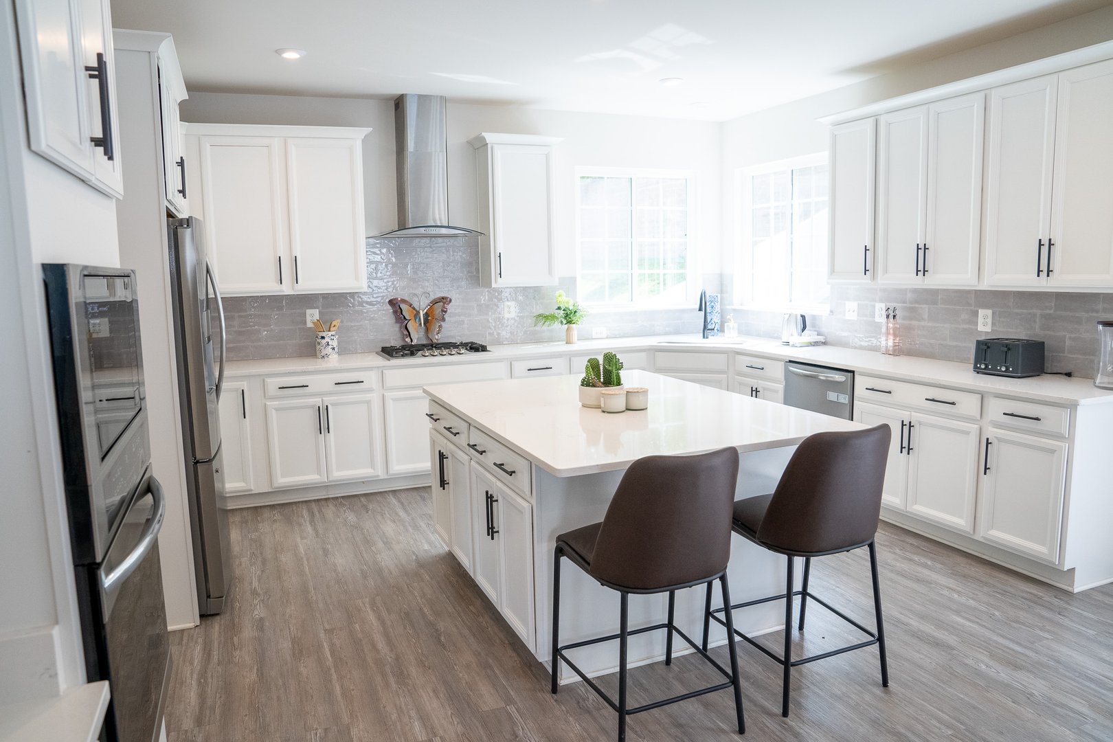 Modern kitchen with white cabinets, stainless steel appliances, and a central island with two chairs.