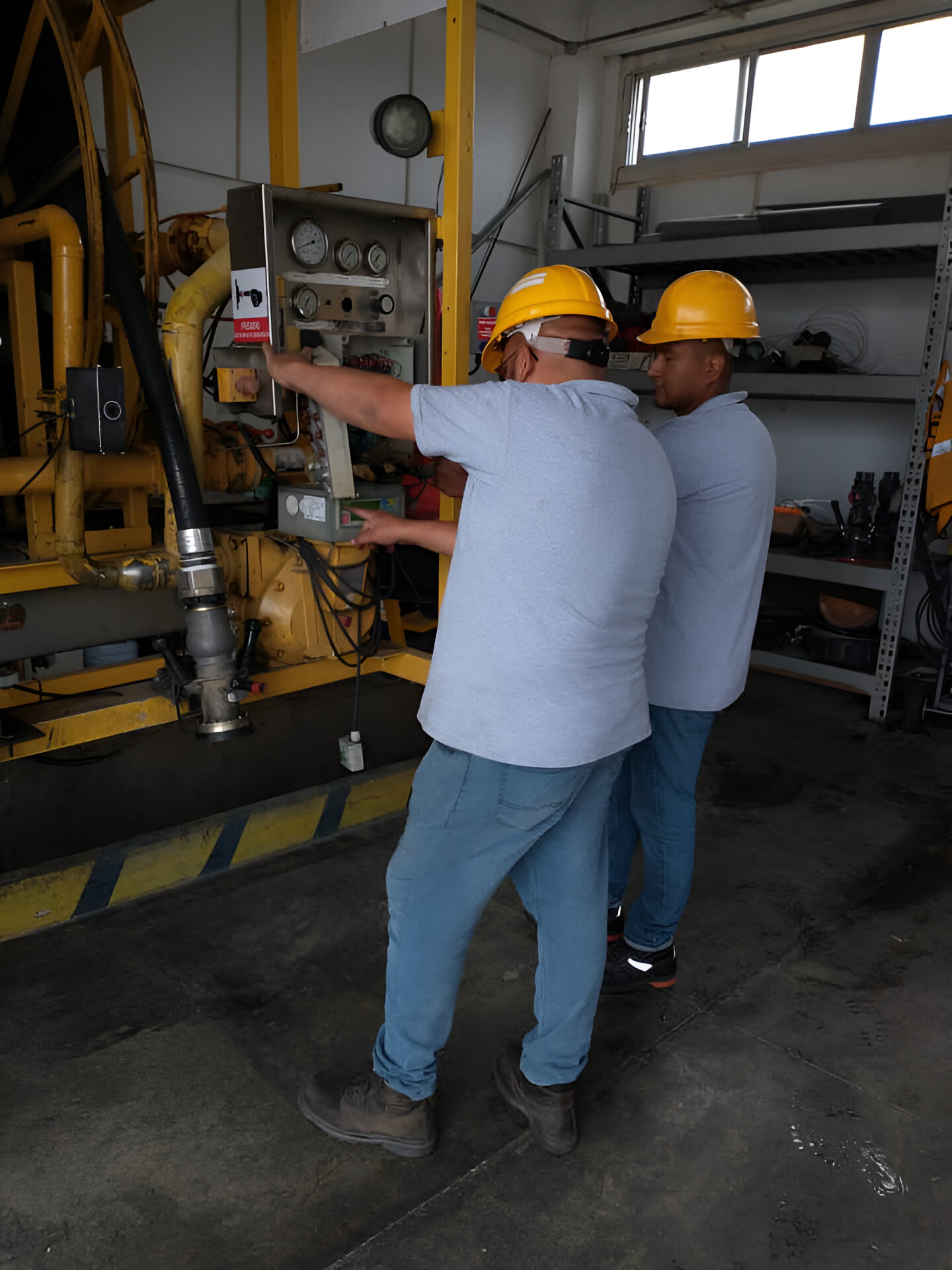 Two workers in hard hats operate machinery controls in an industrial setting, focusing on a control panel.