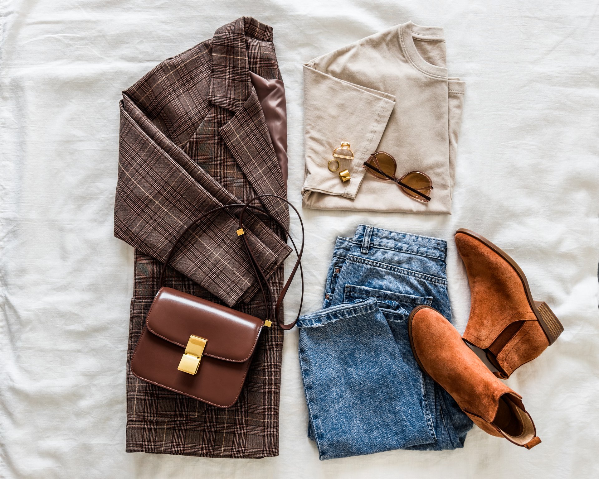 Women's clothing - plaid jacket, t-shirt, jeans, chelsea, cross body bag on a light background, top view