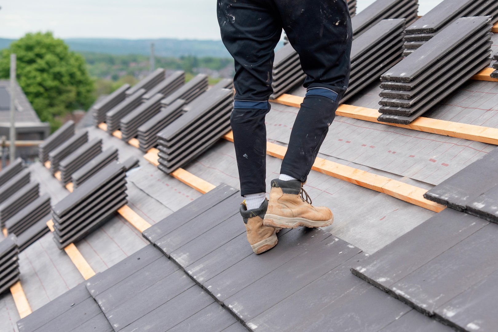 Roofer carefully places slate roofing tiles on a structure's roof ensuring proper alignment and stability