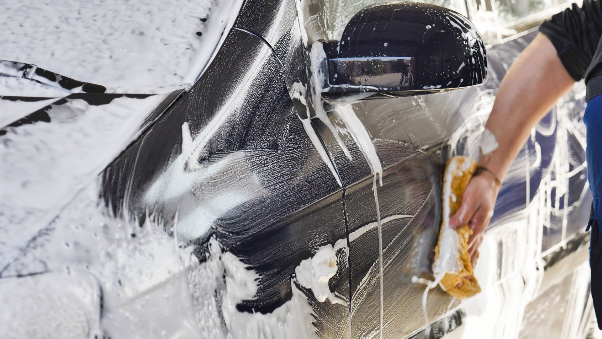 Car wash worker is cleaning a vehicle with a sponge and soap
