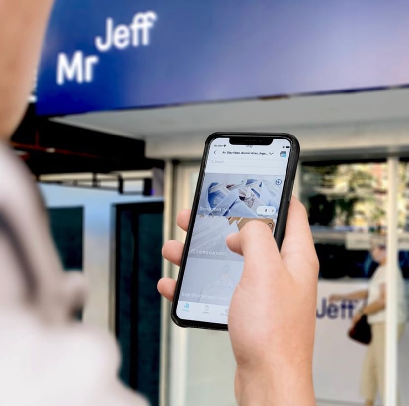 Person using a smartphone app in front of a building with a blurred sign reading Jeff.