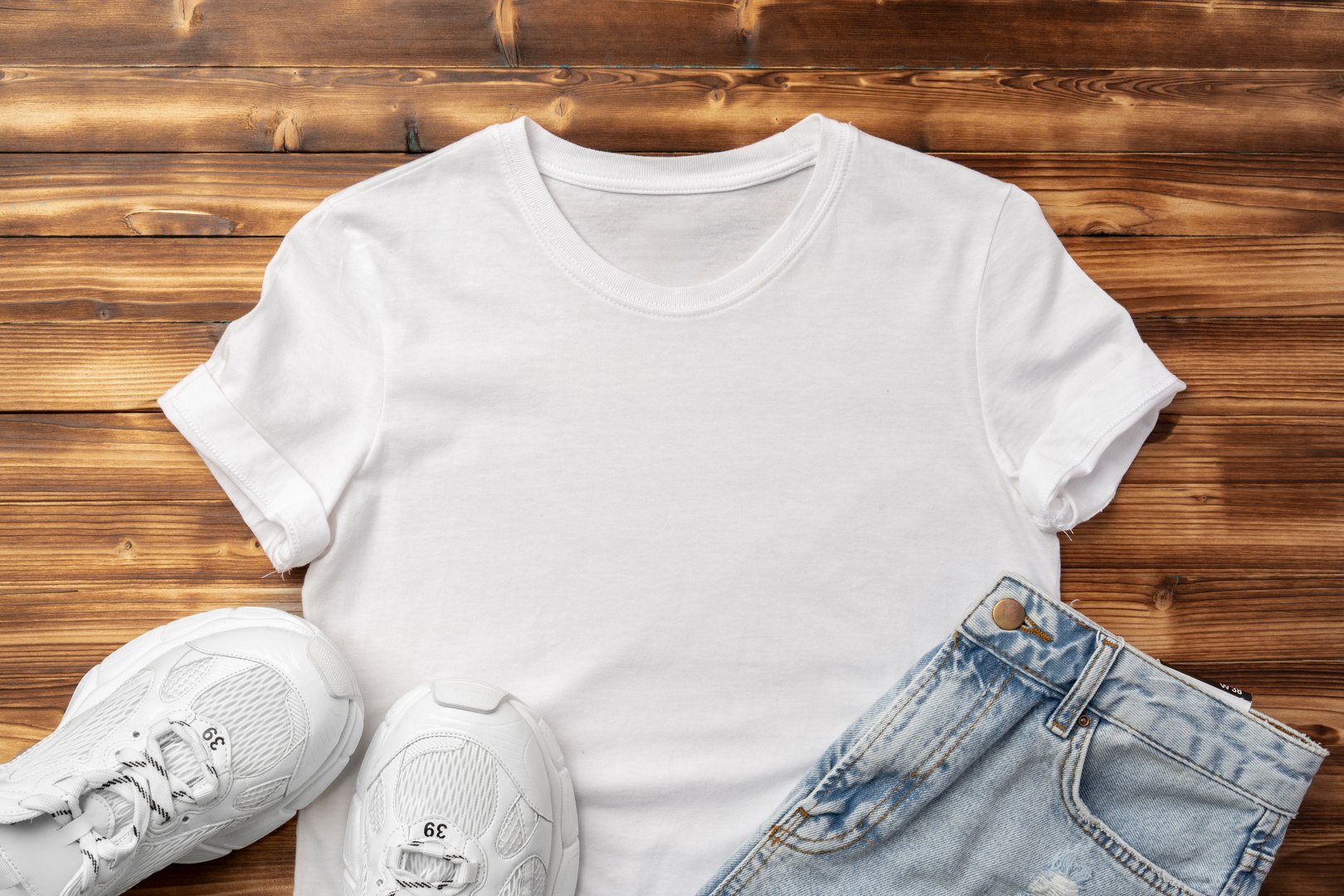 Cotton T-shirt, jeans and sneakers on wooden background top view flat lay
