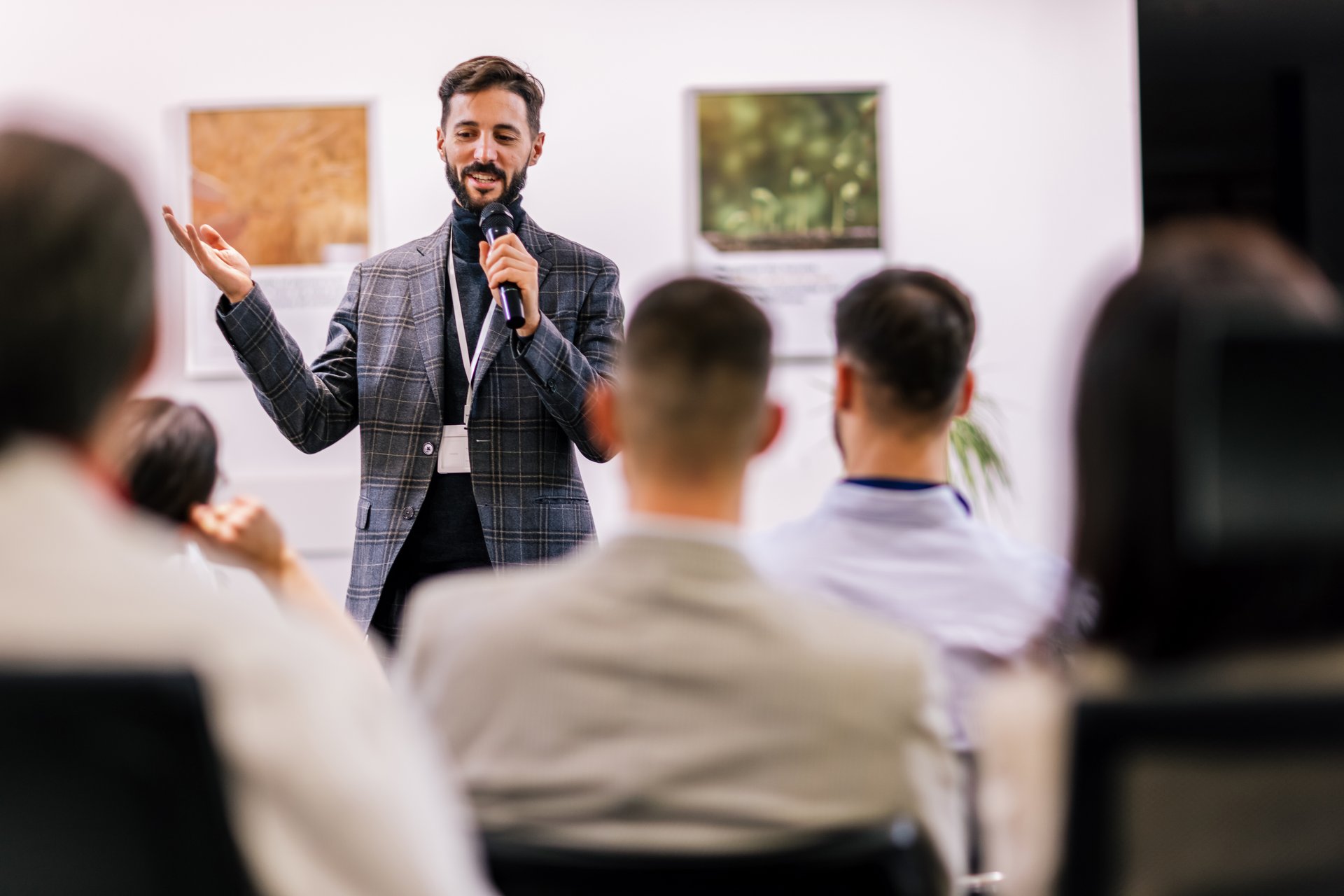 Young business man lecturing his multiethnic colleagues. Having a speech while holding a microphone. Everyone is listening and some are raising their hand.