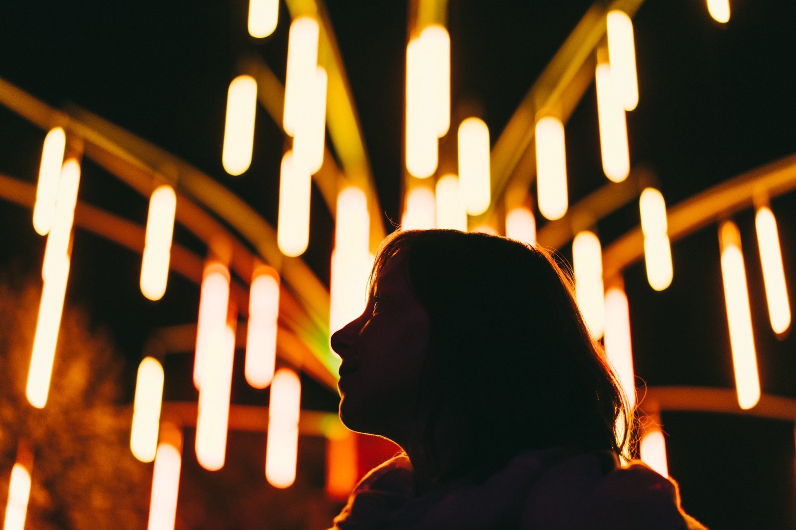 Silhouette of a person facing colorful vertical light installations against a dark night background.