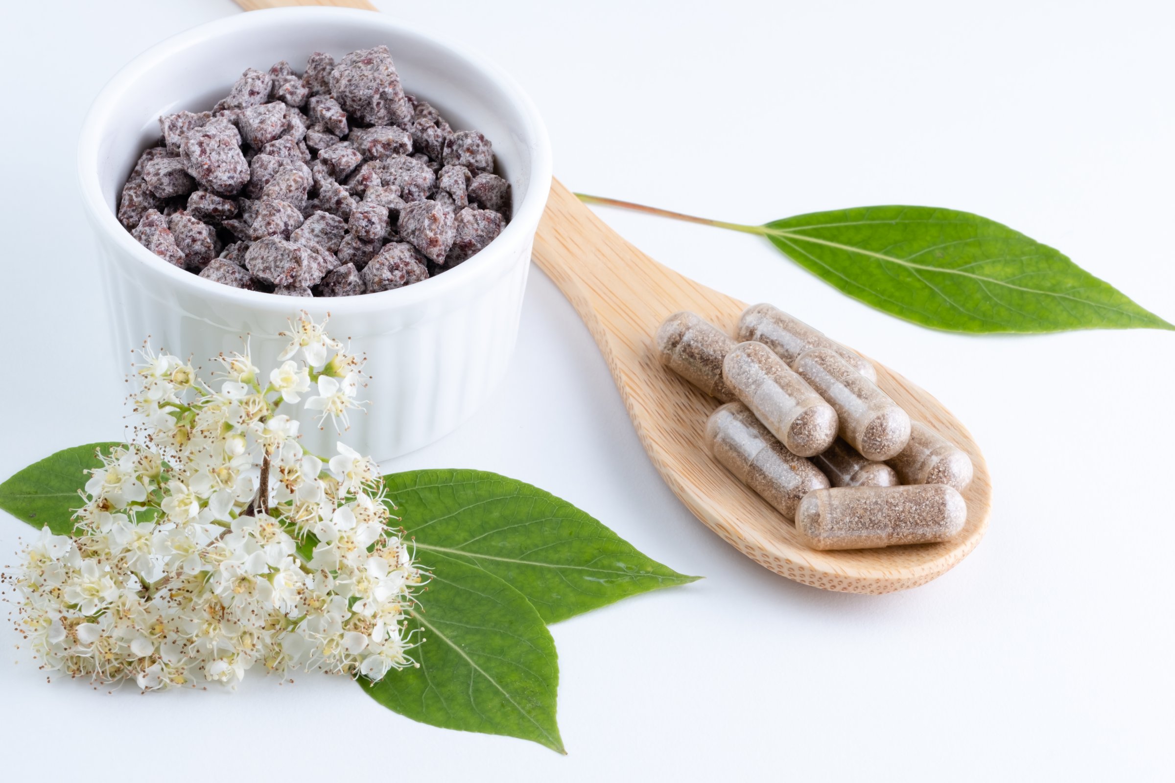 Natural supplements a white bowl surrounded by green leaves and white flowers on a light background. Alternative medicine, healthy and well-being theme concept. top view
