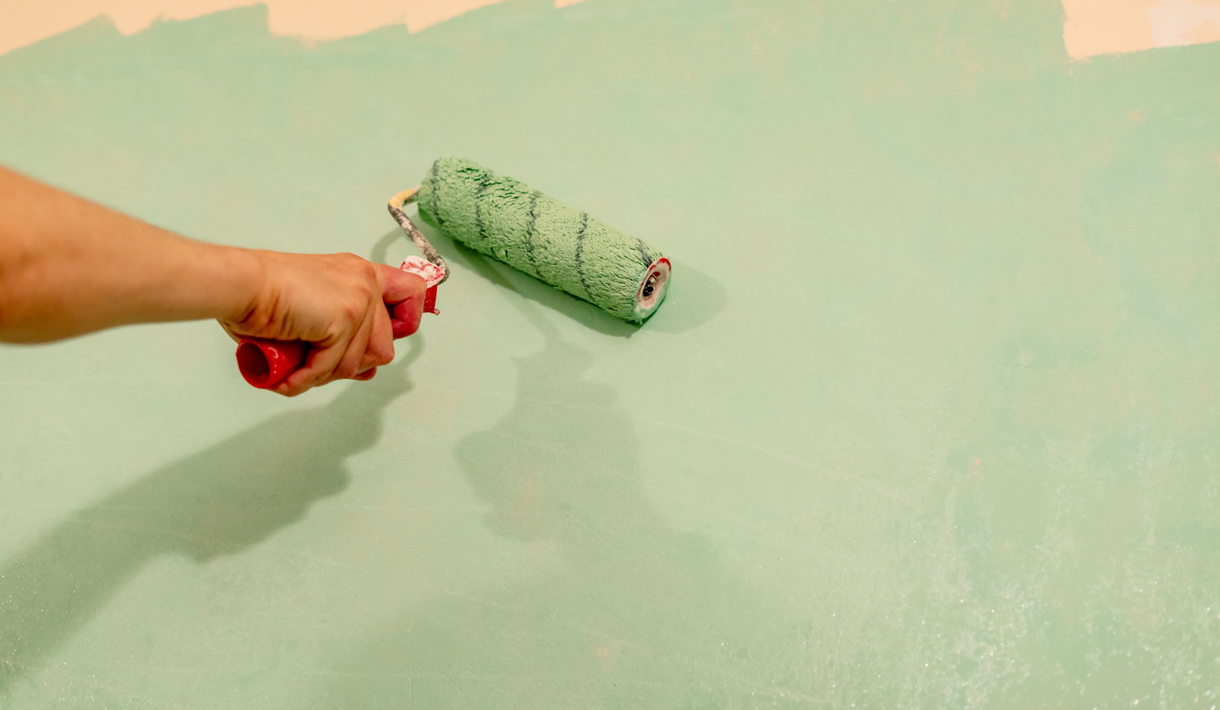 Individual using a paint roller to apply green paint on a wall, demonstrating home improvement skills and creativity in a renovation project