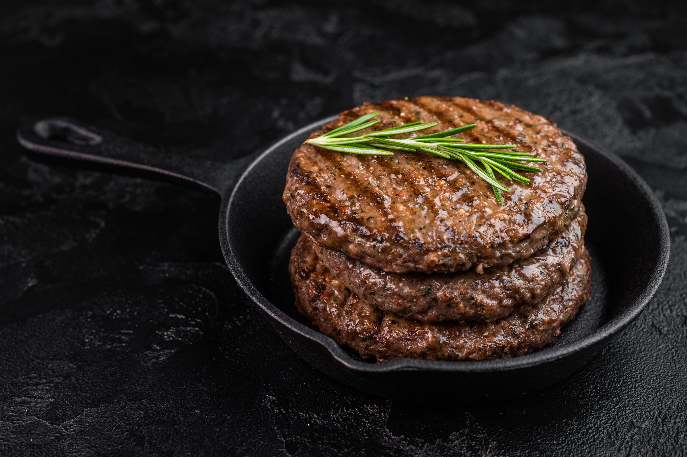 Grilled beef and lamb hamburger patty with seared crust and juicy texture in cast iron skillet.