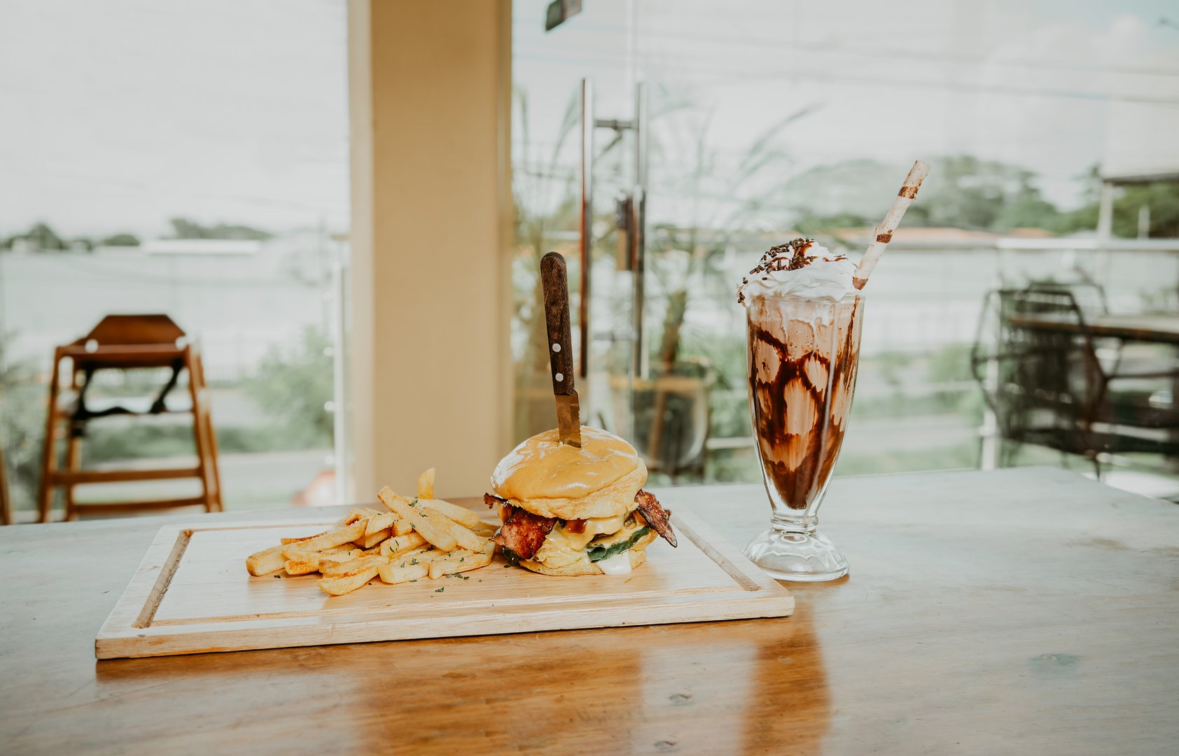 Delicious big burger with french fries and milkshake on restaurant table. Close up of burger with fries and milkshake on wooden board with space for text