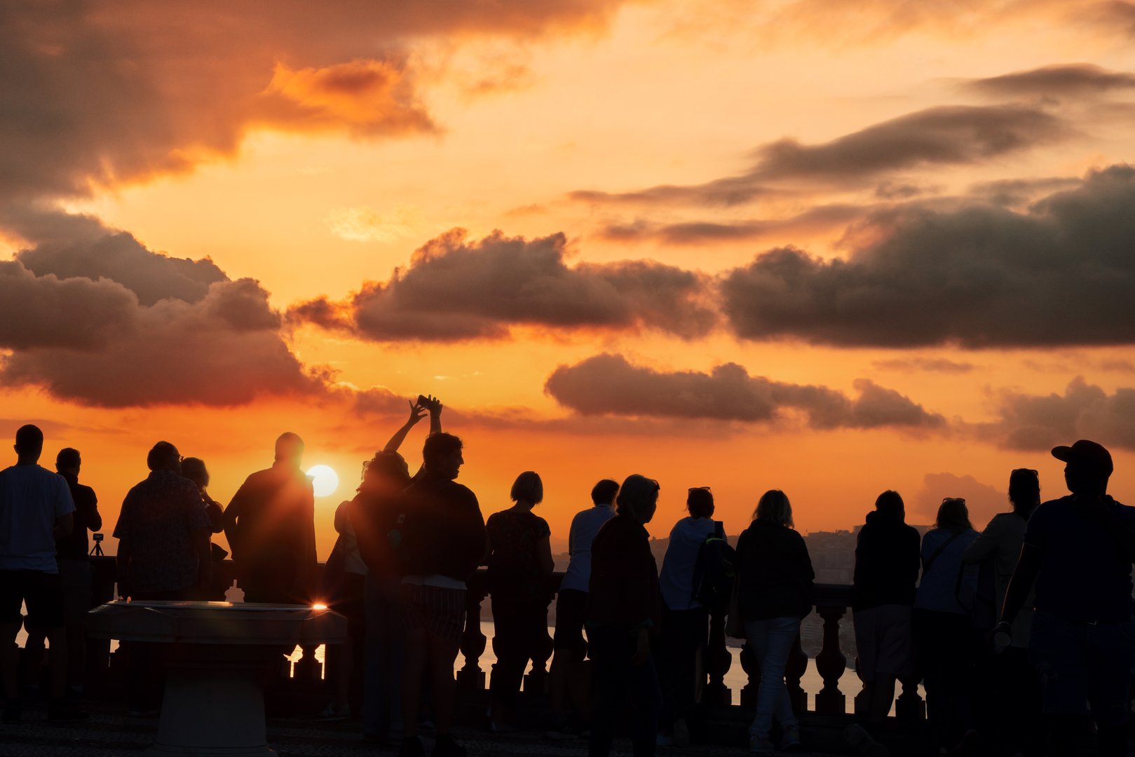 Silhouettes of people enjoying a breathtaking sunset on a scenic viewpoint overlooking the sea and the promenade of Nice