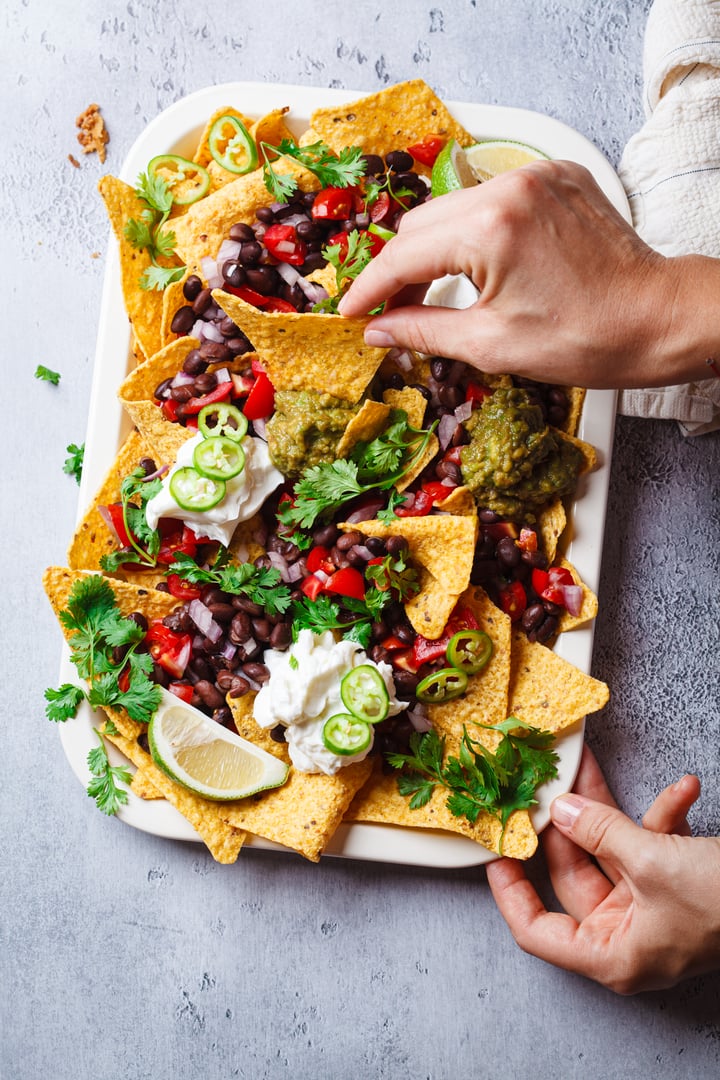 Woman eating vegan nachos with guacamole, black beans and salsa for party, top view.