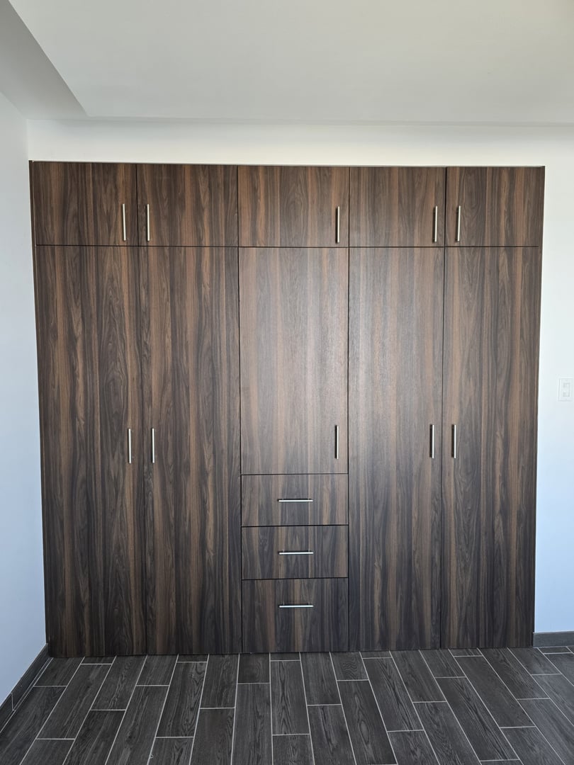Wooden built-in wardrobe with multiple doors and drawers, featuring modern silver handles, against a tiled floor.