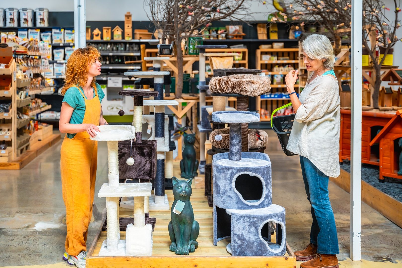 Shop assistant is showing different scratching posts to a customer in a pet shop, helping her choose the right one for her cat