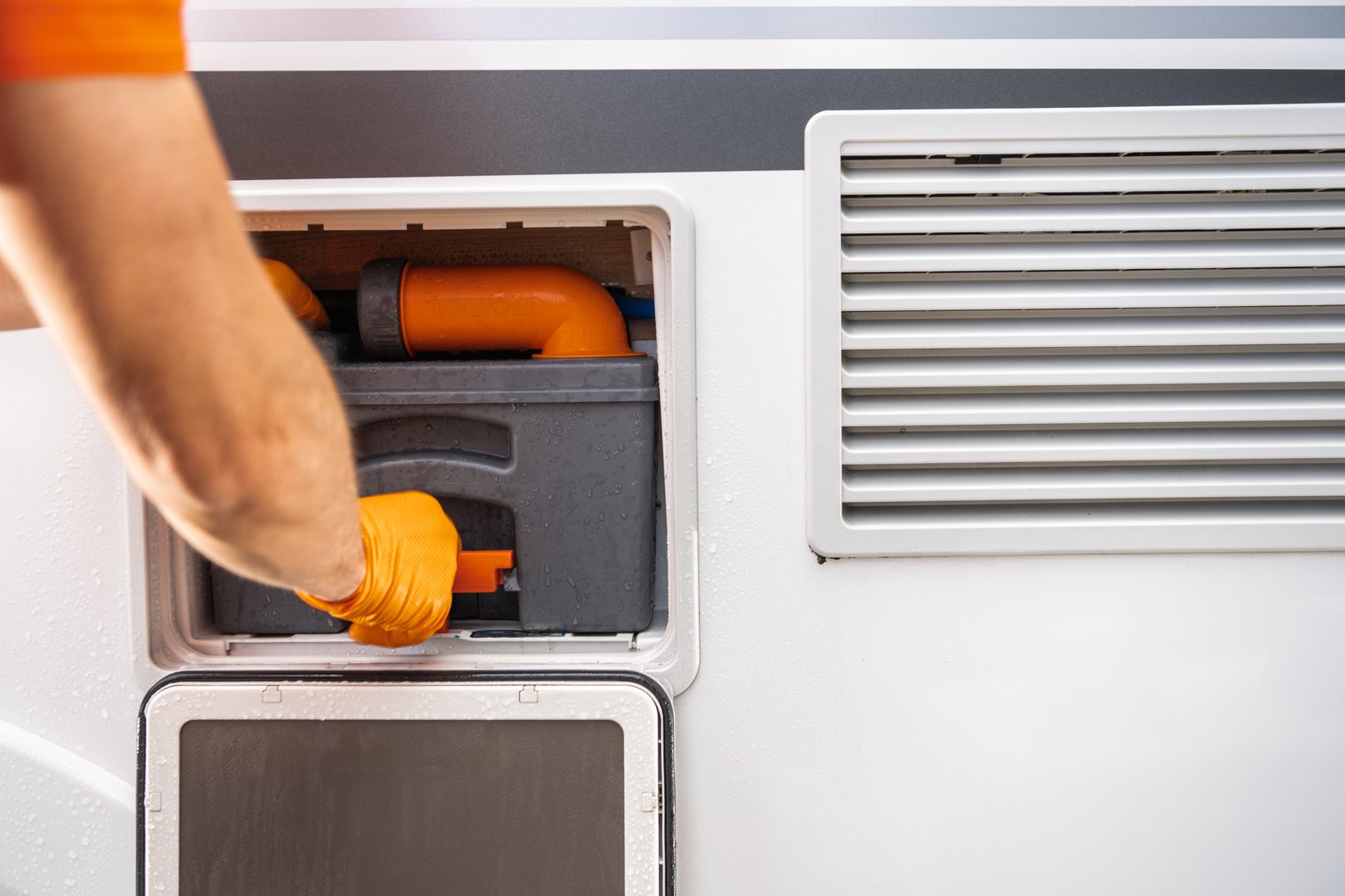 A person is opening the utility compartment of a camper van, revealing RV toilet cassette