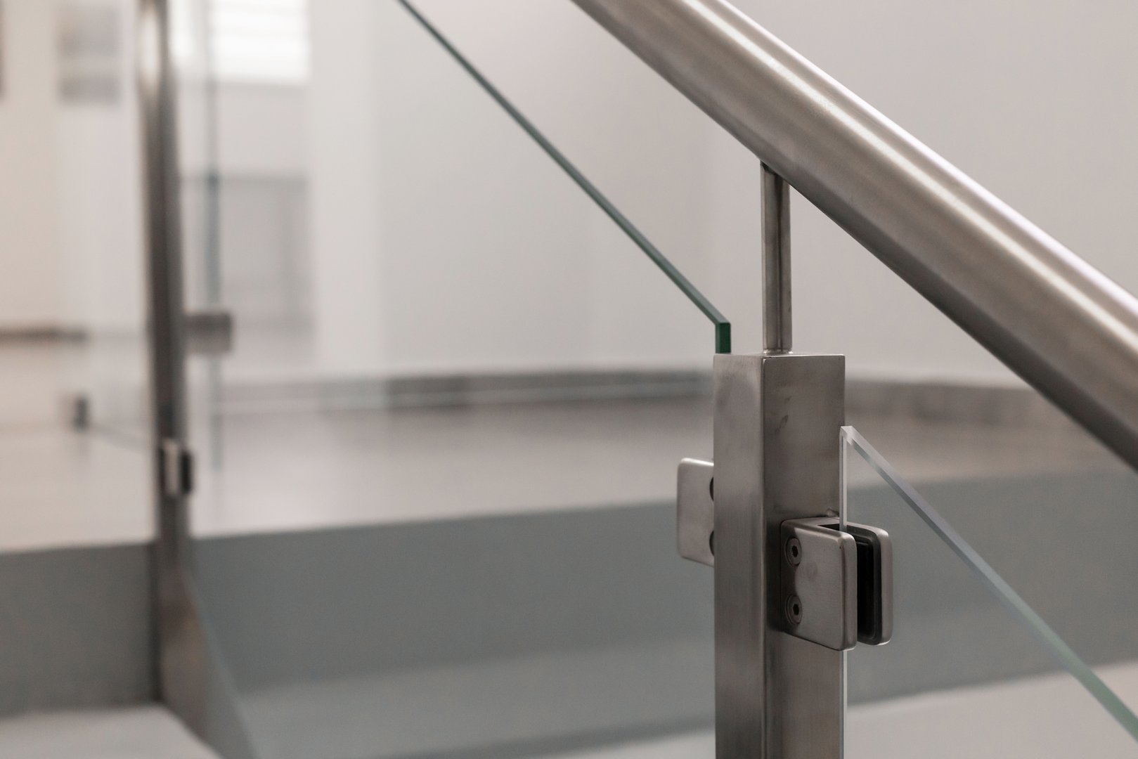 Close-up view of a sleek metal and glass railing, showcasing modern architectural details in a bright, minimalist interior space during daylight hours.