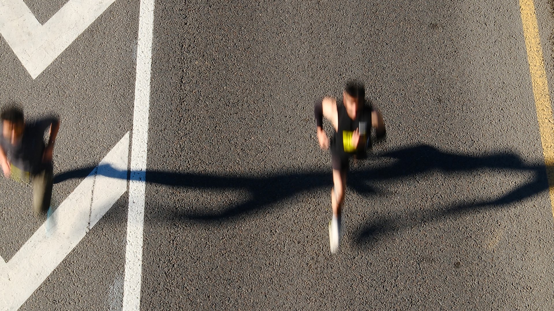 Aerial view of marathon runners on urban road with chevron markings, blurred motion capturing speed and movement of competitors