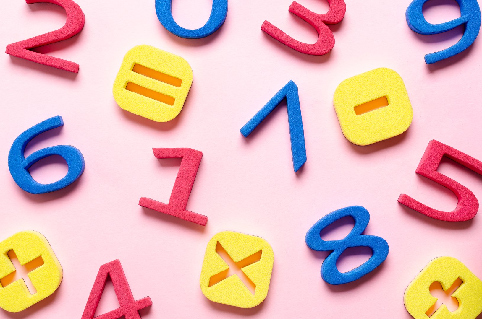 Pattern of colorful foam numbers and math symbols on pink background.
