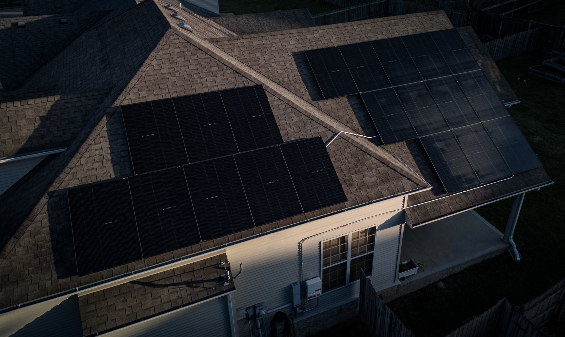 A residential home's rooftop features a photovoltaic system, with wiring and cables extending to an externally mounted inverter and a quick disconnect device.