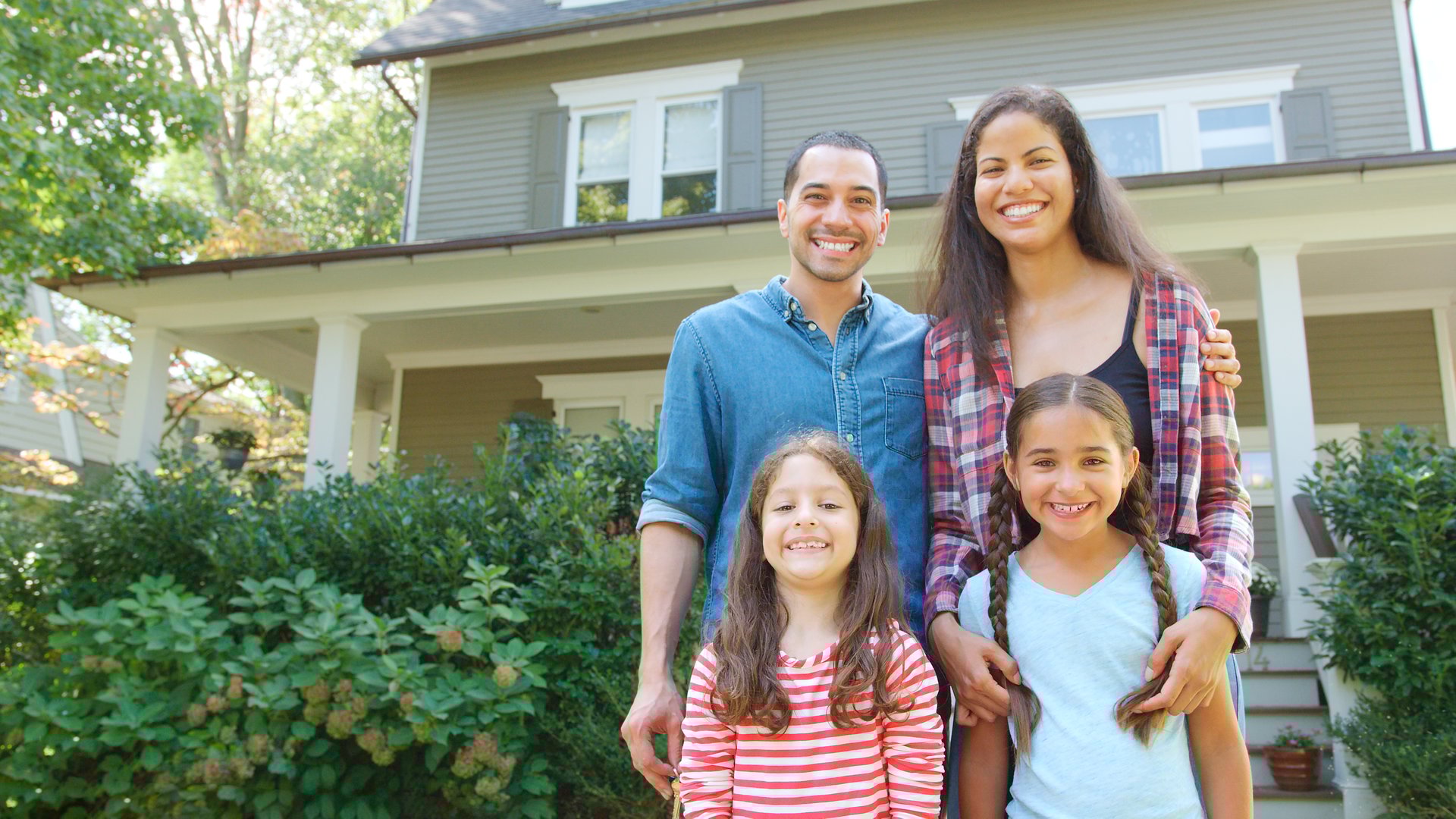 Portrait Of Smiling Family Standing In Front Of Their Home