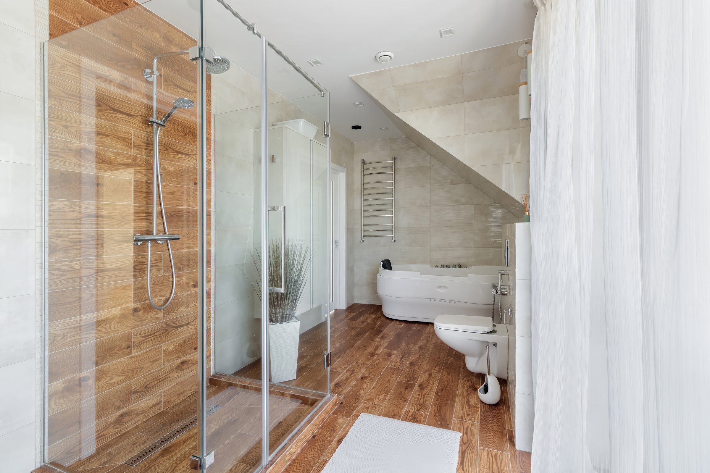 A modern bathroom featuring elegant fixtures, wooden floors, and ample natural light for a serene and spa-like atmosphere.