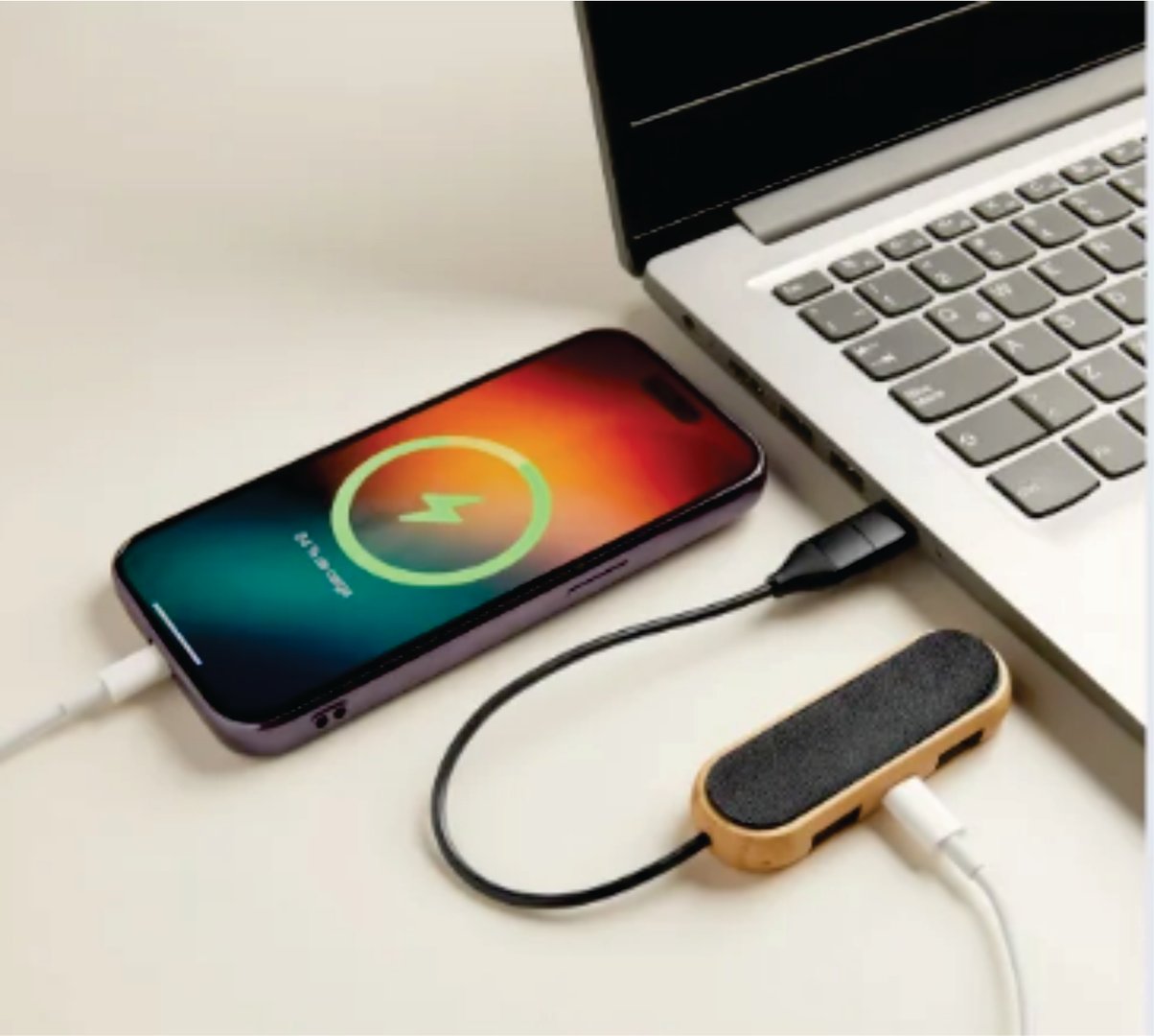 A smartphone charging next to a laptop, both connected by a small power bank with a wooden exterior and fabric top.