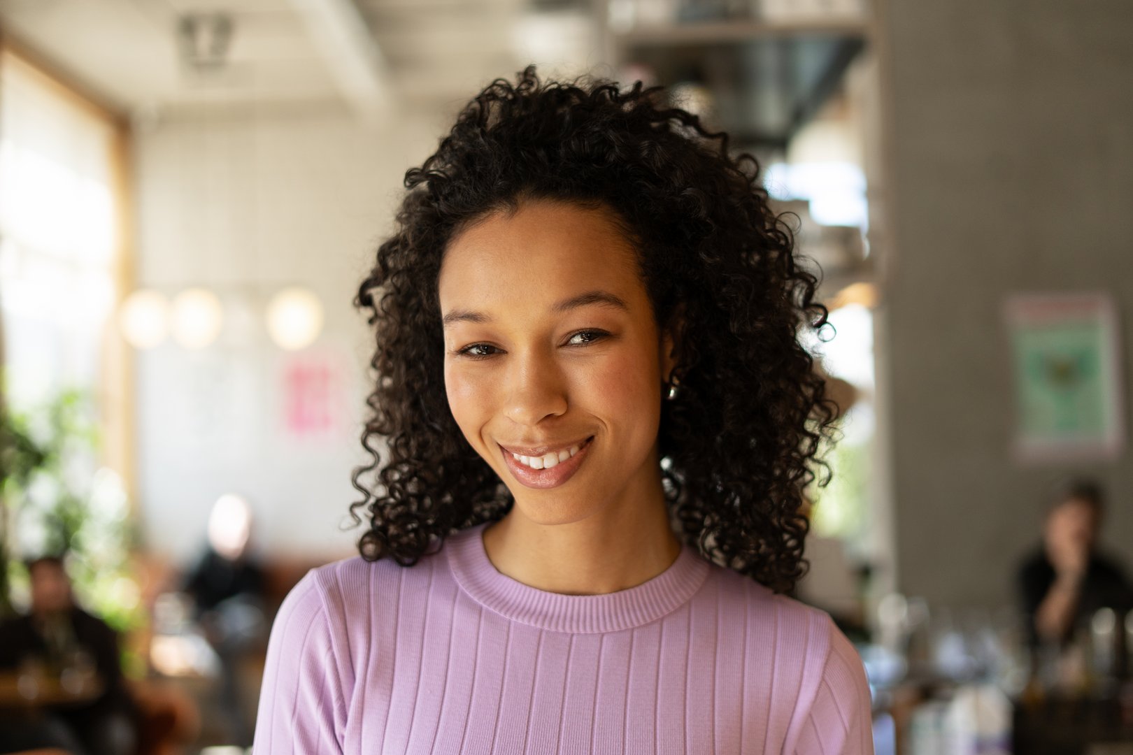 Portrait of a young woman smiling warmly in a cafe, exuding happiness and confidence while enjoying a relaxing moment in her day